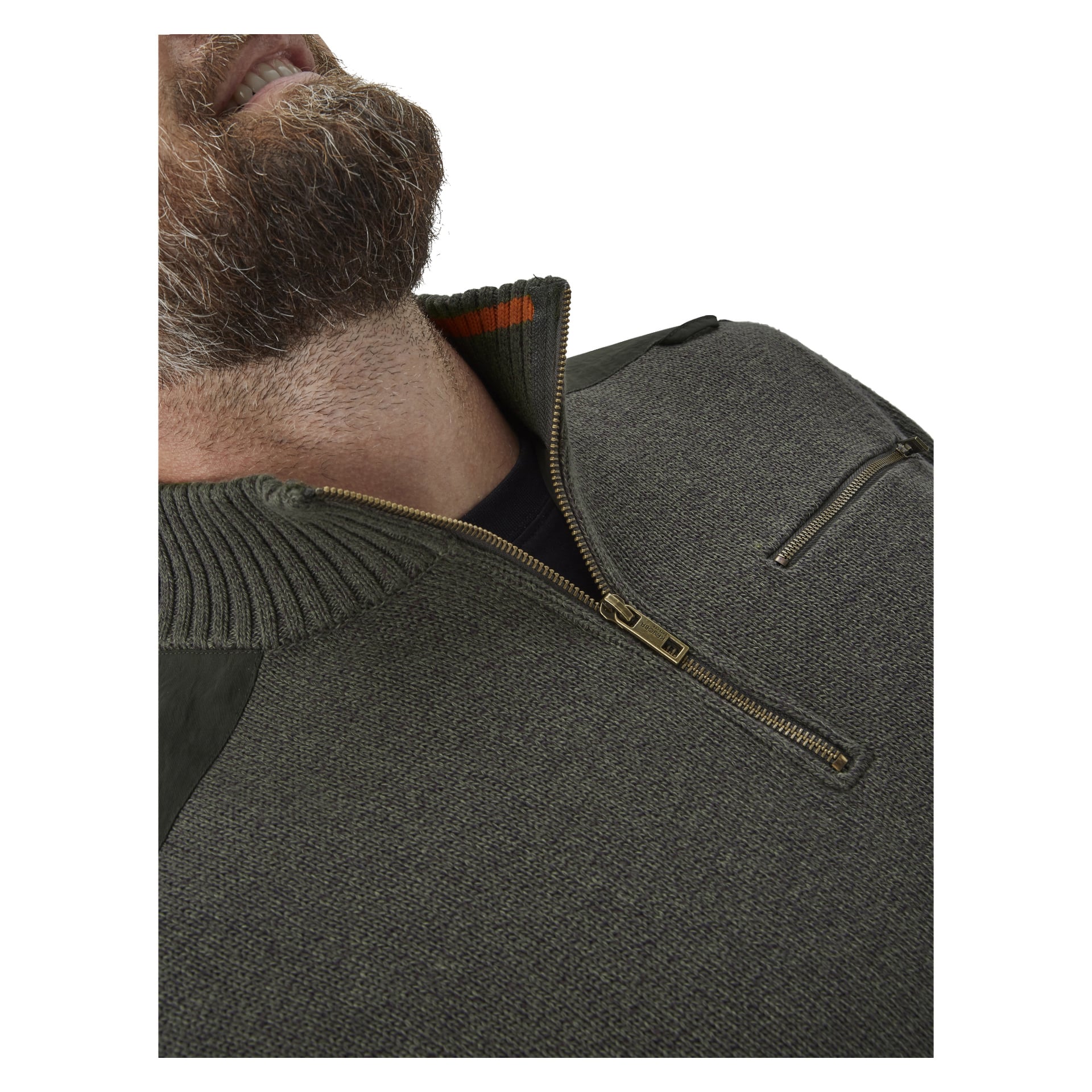 Närbild av en skäggig man i en olivgrön Kayoba Outdoor Knitted Men's Hunting Sweater Cannock, som har en dragkedja och en liten ficka på bröstet. Bilden är tagen från en låg vinkel, vilket drar uppmärksamheten till hans käklinje och hals.