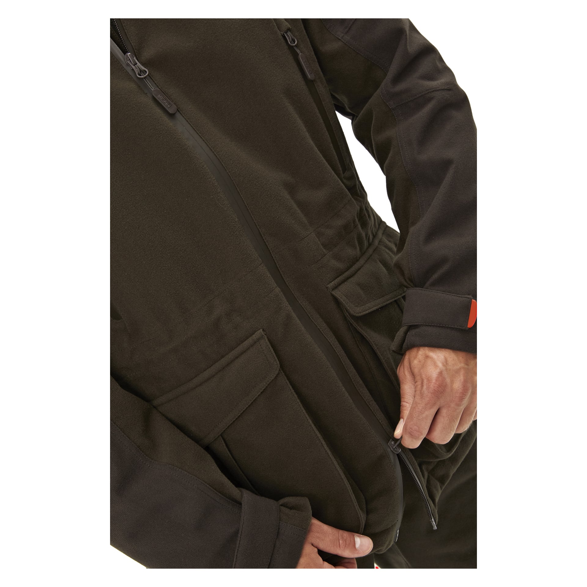 En person är synlig från axlar till midja och knäpper dragkedjan på en mörkbrun Kayoba Outdoor Men's Cannock Superior jaktjacka med höger hand. Jackan har stora framfickor och framträdande sömlinjer.