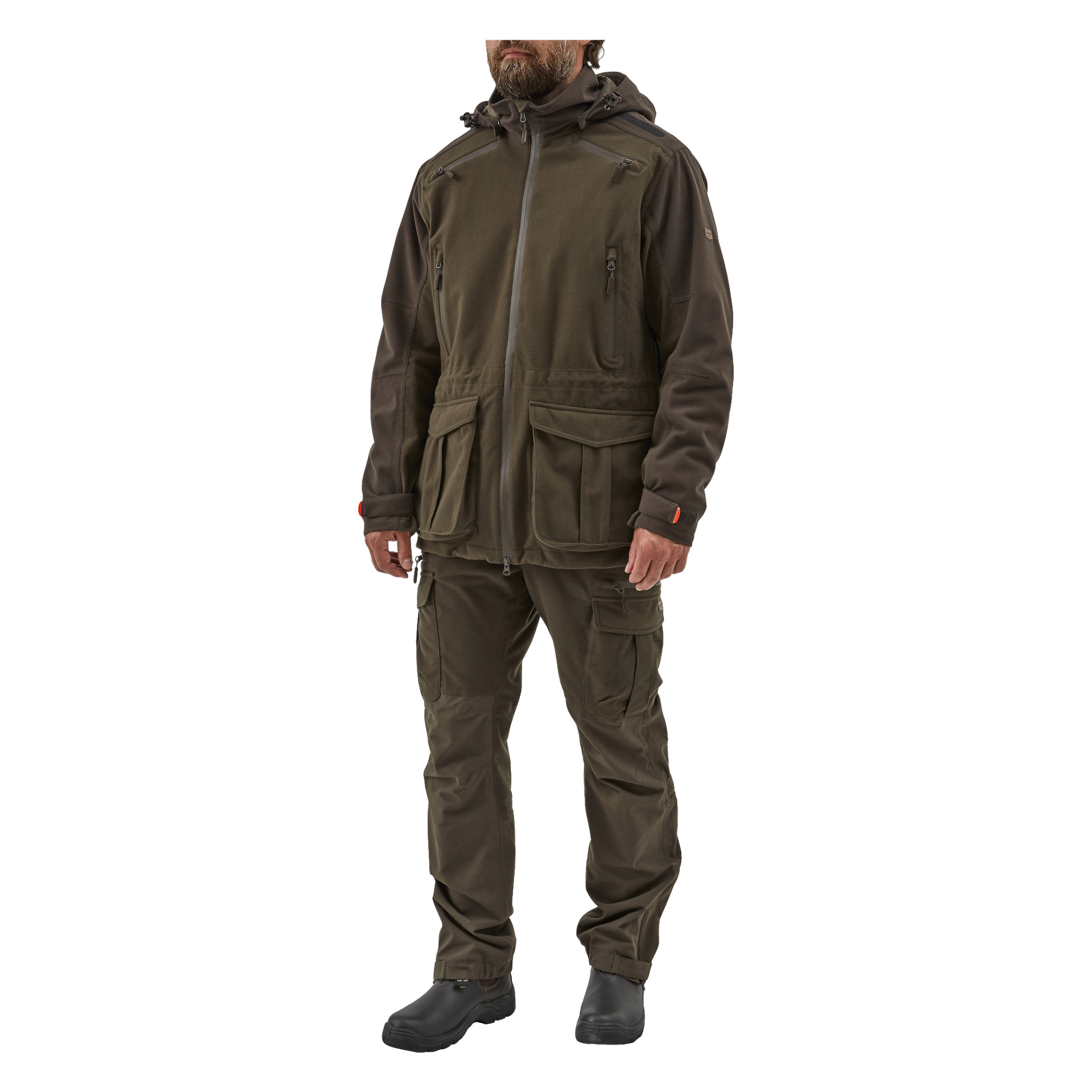 En man vänder blicken framåt, klädd i en olivgrön Kayoba Outdoor Men's Cannock Superior jaktjacka med matchande cargobyxor och svarta stövlar. Hans armar vilar naturligt vid sidorna, och skägget döljer delvis ansiktet.
