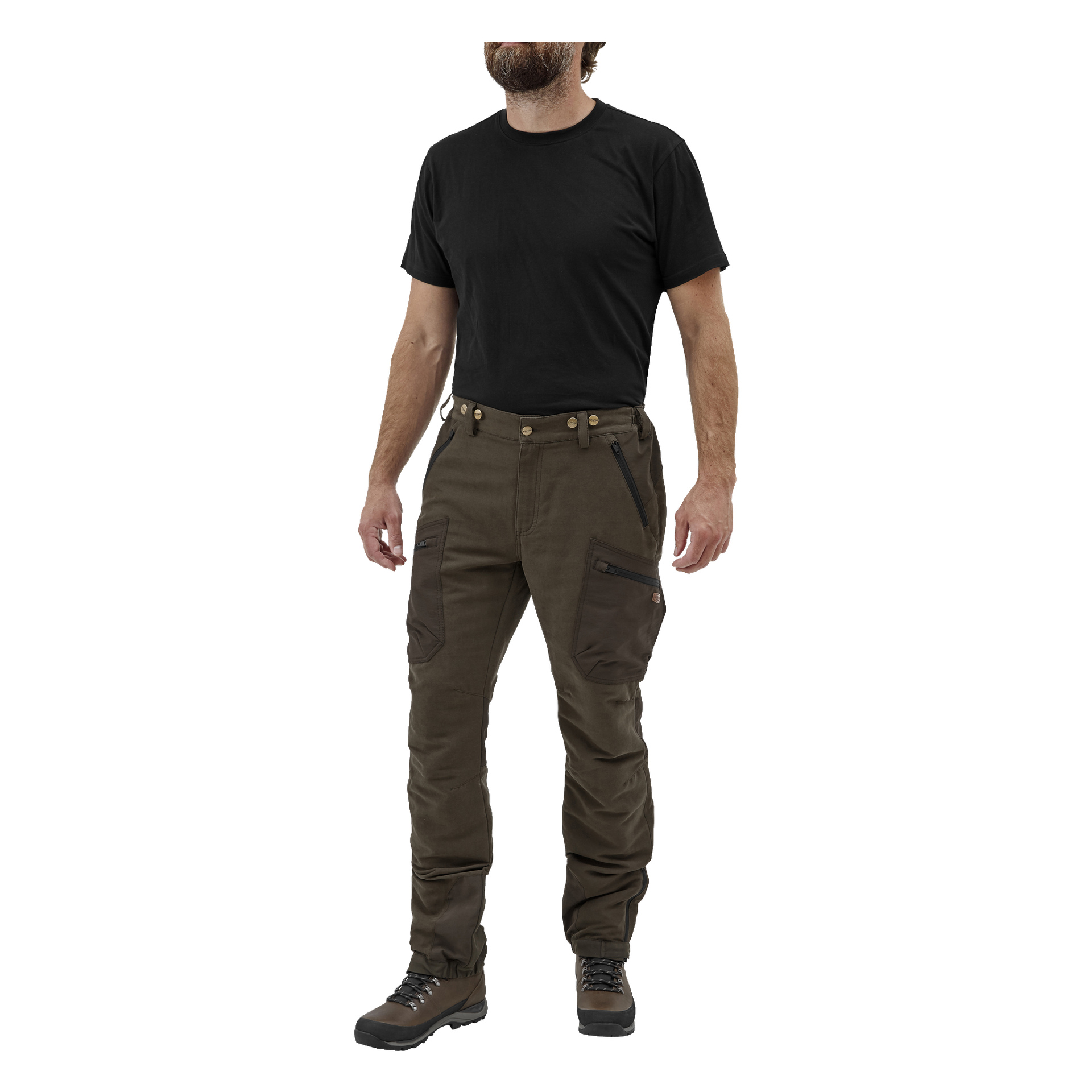 En skäggig man är klädd i en svart t-shirt, Grimsö jaktbyxor från Kayoba Outdoor med förstärkta knän och fickor med dragkedja, samt bruna vandringskängor. Han står i en liten vinkel med armarna bekvämt vilande vid sidorna.