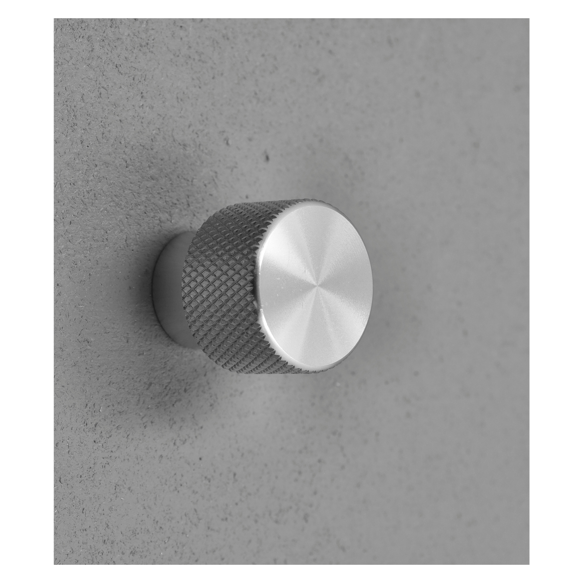 Et detaljert bilde av en Hard Head Knob 2-pakke har runde, metallknotter med teksturerte sider og børstede topper, montert på en grå, teksturert overflate og vist fra en liten vinkel.