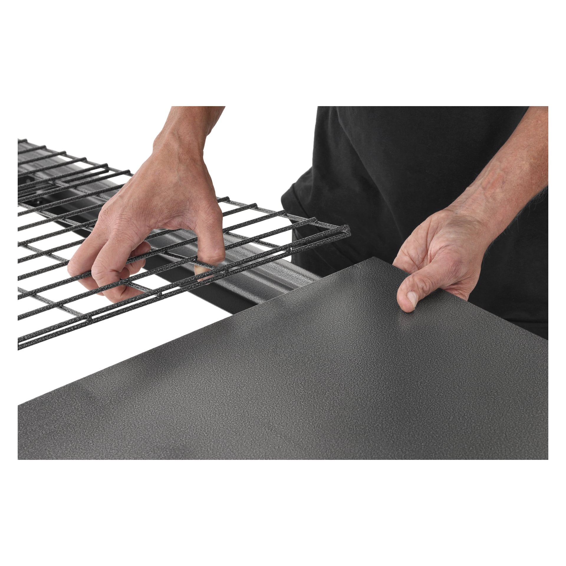 En persons händer monterar Hard Head Wire Shelf Modular Storage System på en texturerad metallpanel och placerar noggrant komponenterna. Endast händerna och delar av deras armar kan ses.