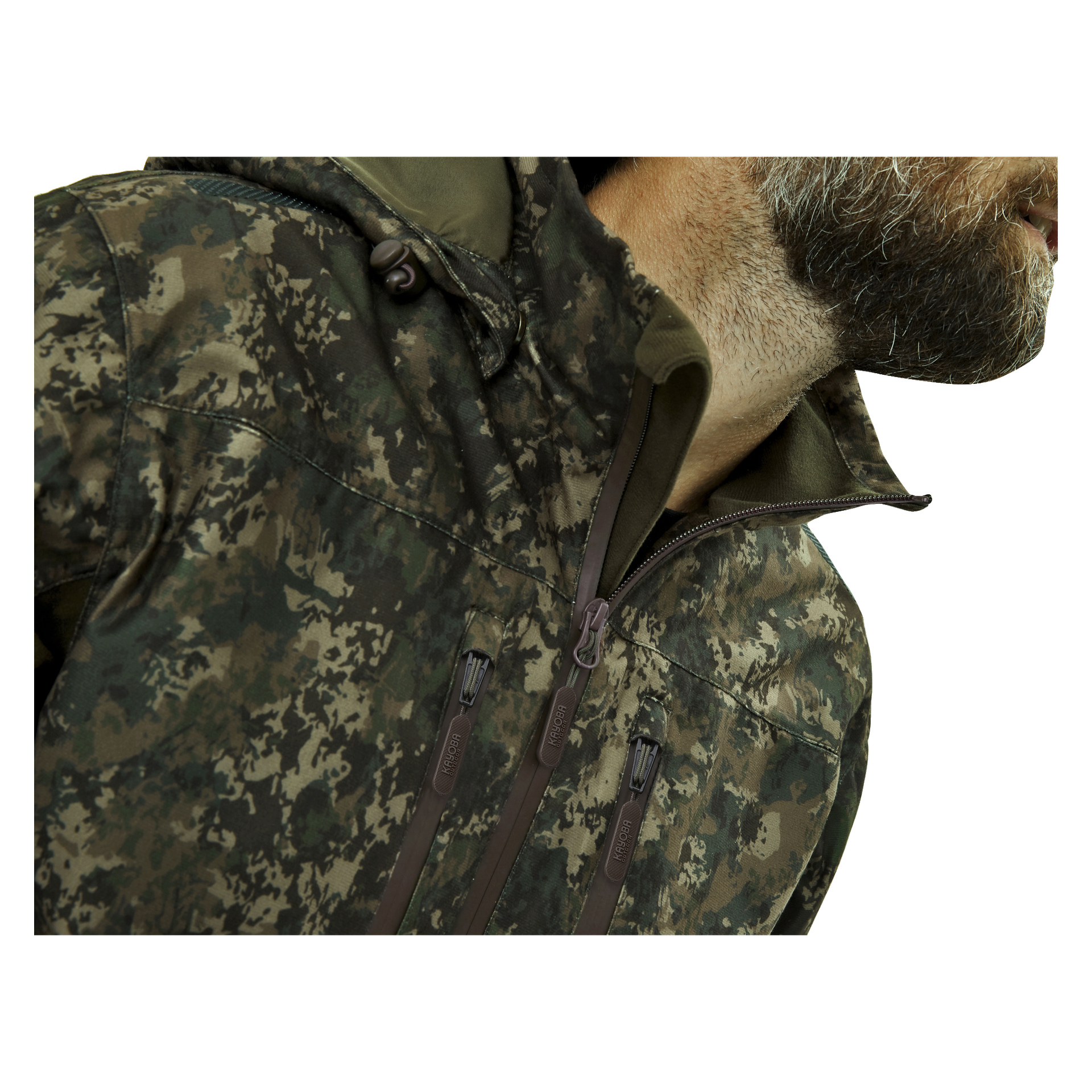 Närbild på en person klädd i Kayoba Outdoor Men's Cannock Camo jaktjacka, som har flera dragkedjor. Endast deras skägg och den nedre delen av ansiktet är synliga. Ljussättningen är jämn genom hela bilden.