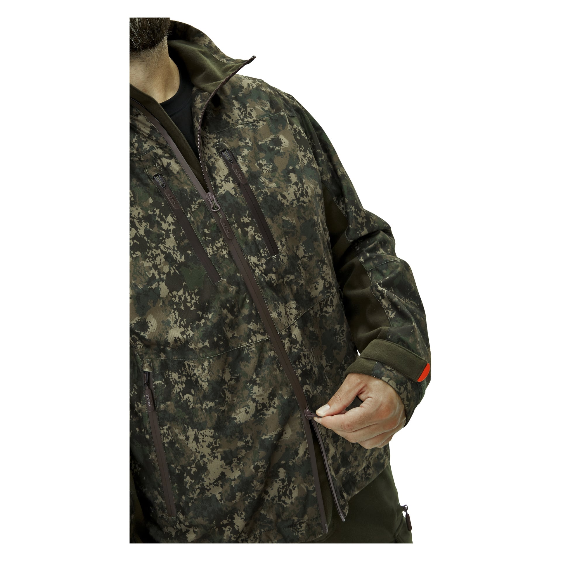 En person drar ner dragkedjan på framsidan av en Kayoba Outdoor Cannock Camo jaktjacka för herrar, med endast överkroppen och handen på dragkedjan synliga, och en del av ansiktet delvis synligt.
