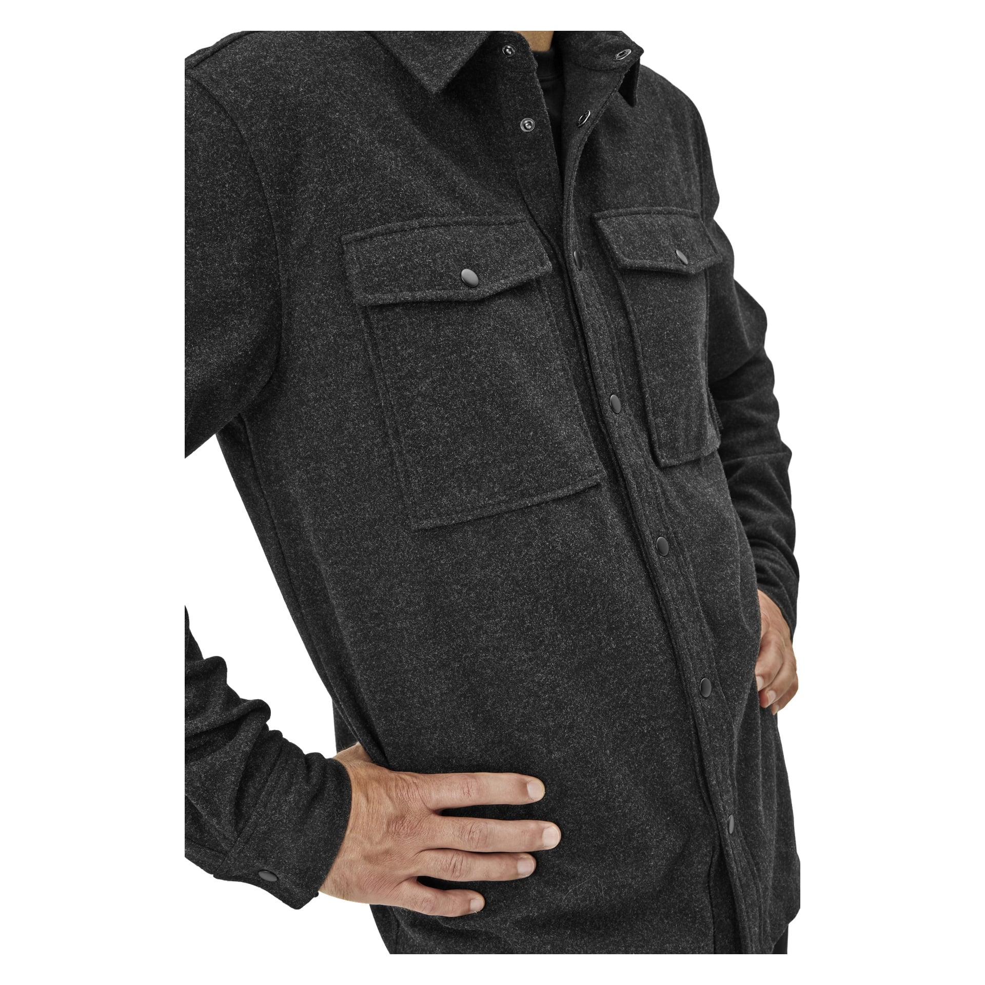 Osoba jest widoczna w Kayoba Outdoor Overshirt Idhult dla mężczyzn, ciemnoszarej koszuli na guziki z dwoma kieszeniami na piersi i zatrzaski, stojącą z jedną ręką na biodrze, a jej twarz nie jest widoczna.