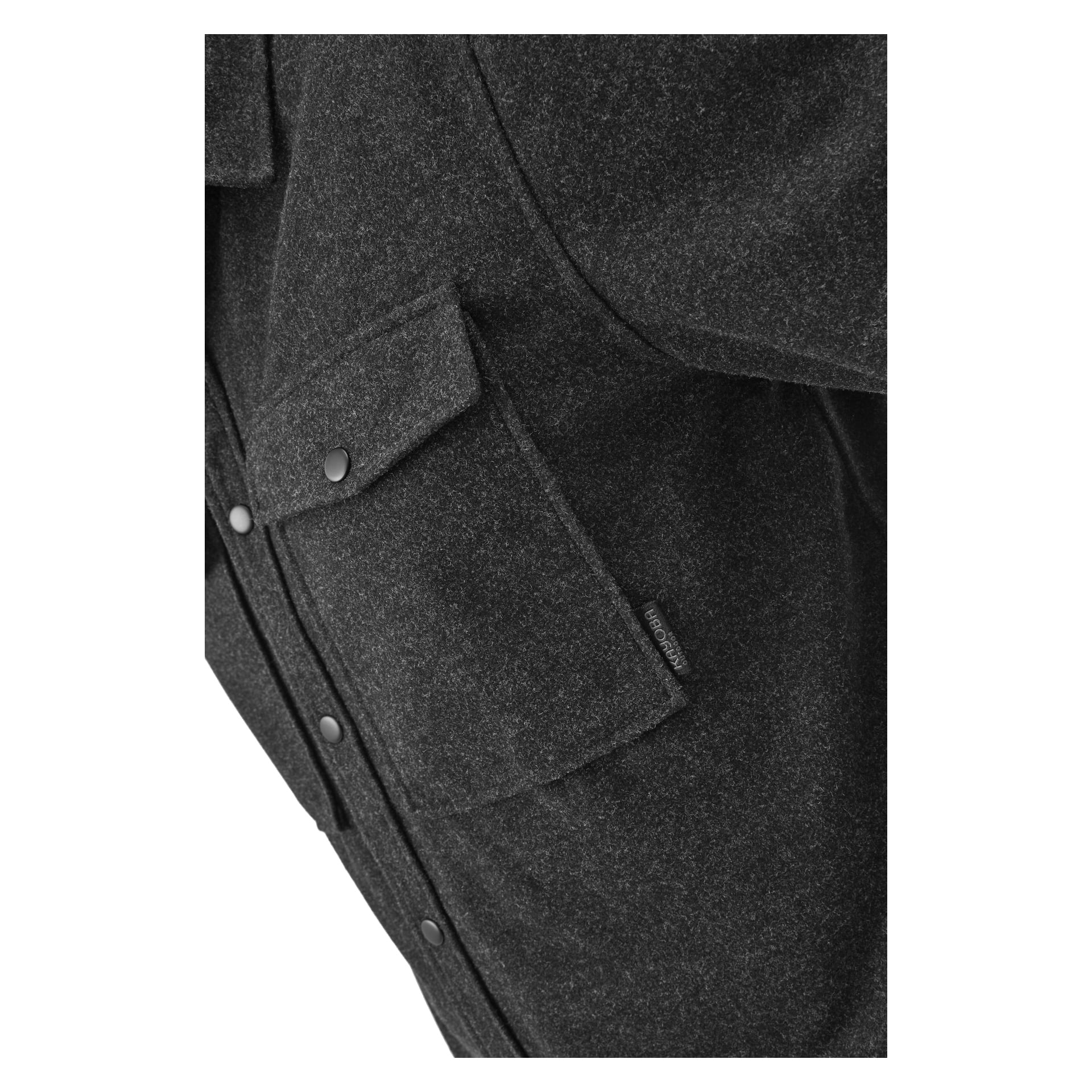 Zbliżenie na "Overshirt Men" Idhult autorstwa Kayoby Outdoor w ciemnoszarym kolorze, pokazujące dwie kieszenie na piersi z zatrzaskami i małą czarną metkę; wykonane z miękkiej, fakturowanej tkaniny.