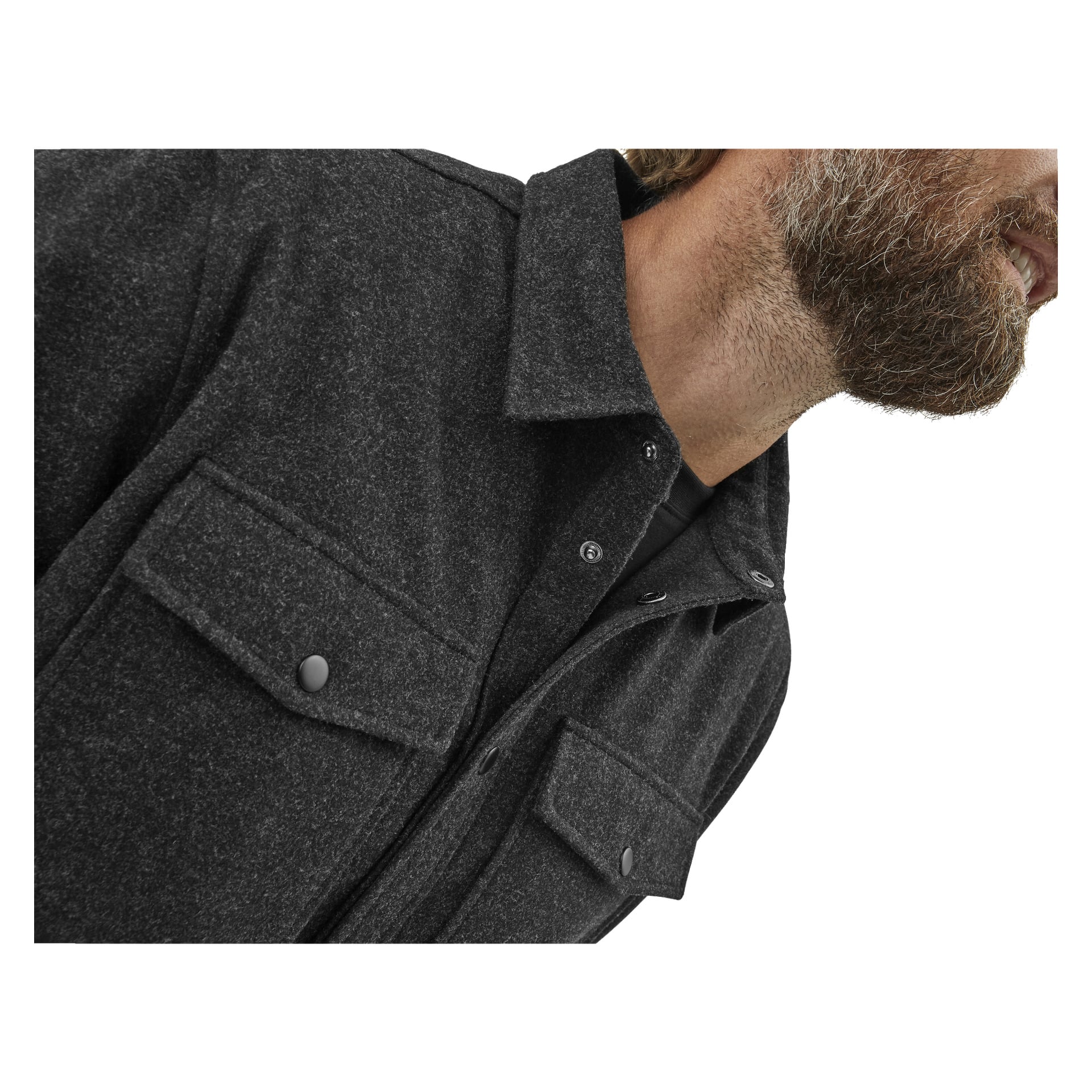 Lähikuva miehestä, jolla on ruskea parta ja joka pukeutuu tummanharmaaseen Kayoba Outdoor Overshirt Men Idhultiin, jossa on läppätaskut rintakehässä, näytettynä leuasta ylärintaan.