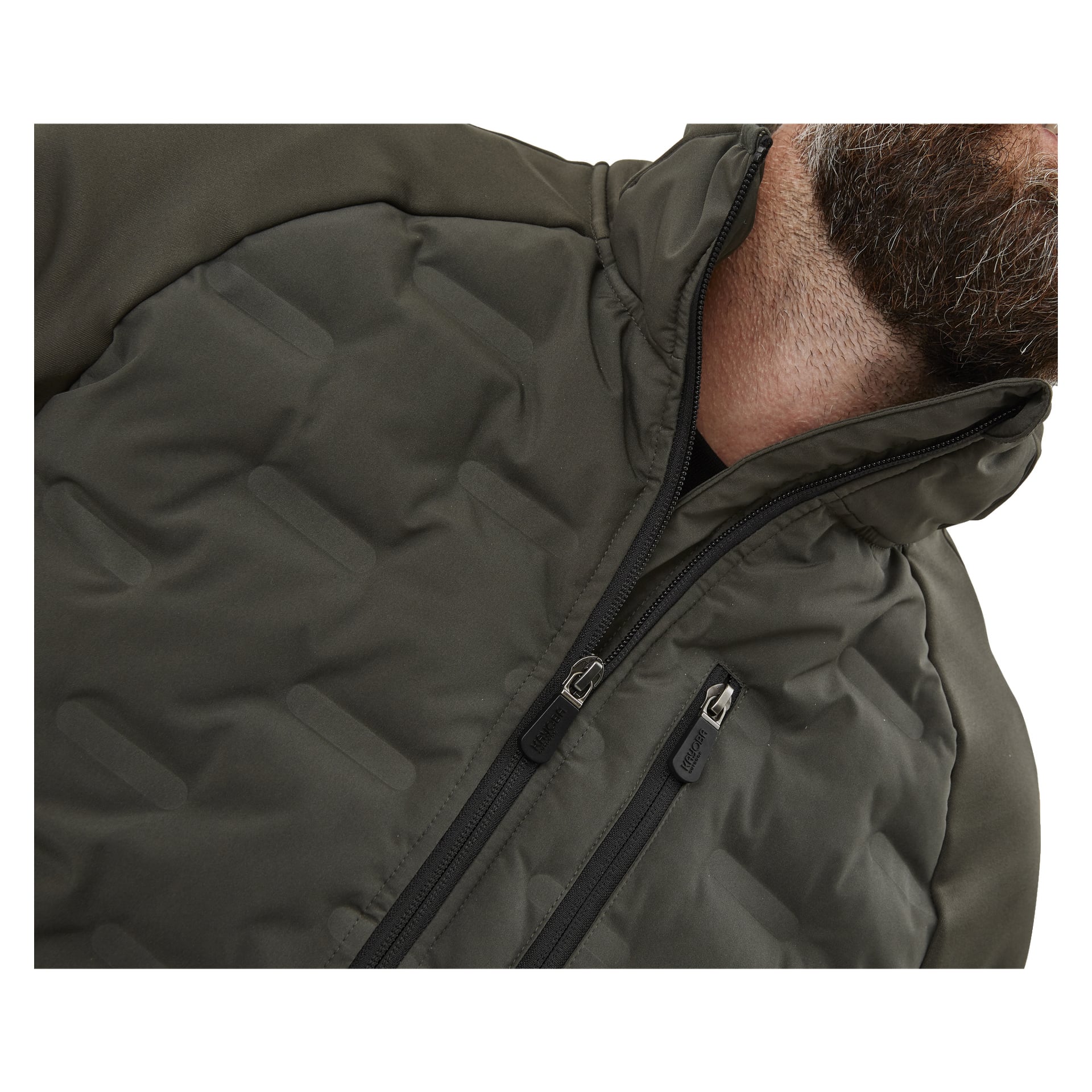 En närbild visar en person i Kayoba Outdoor Men's hybridjacka Särna, som har en mörk quiltad look, två dragkedjor och en upphöjd krage. Endast den nedre delen av deras skäggiga ansikte syns.