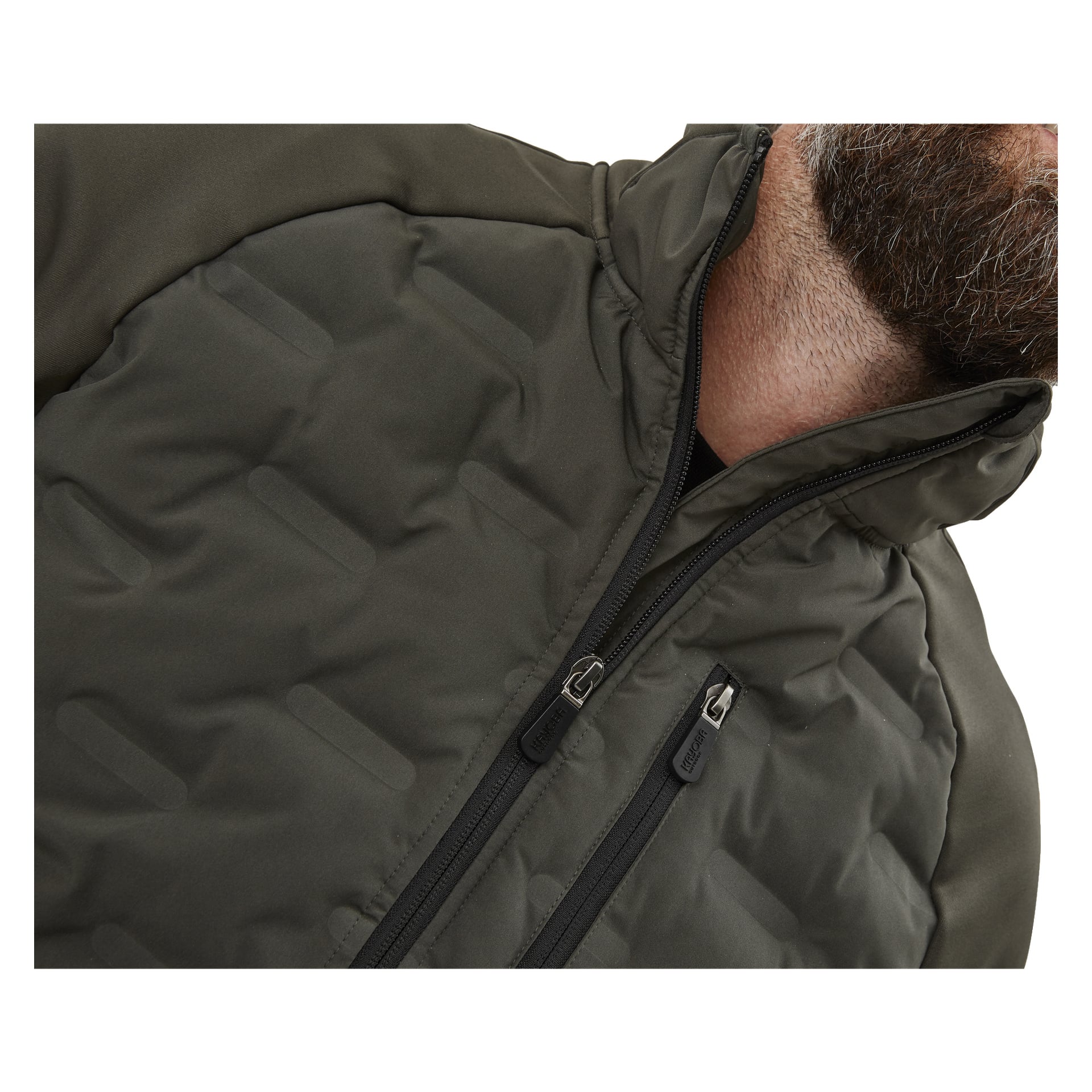 En närbild visar en persons övre bröst, hals och skägg klädd i Kayoba Outdoor Men's Särna hybridjacka. Jackan är quiltad i mörkolivgrönt med hög krage och två dragkedjor—en i mitten och en på bröstet.