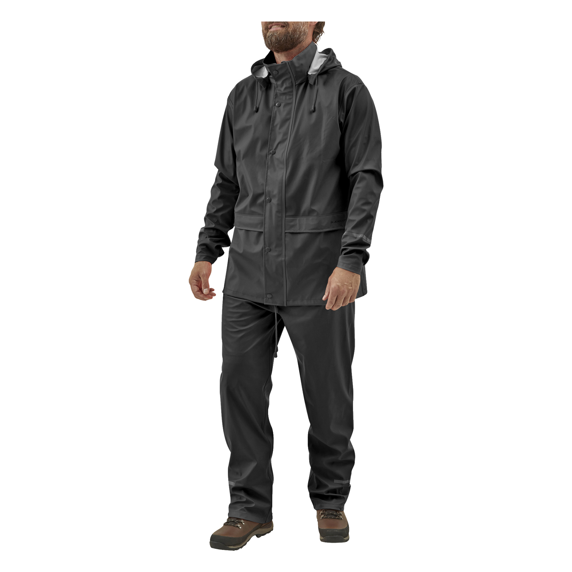 Ein bärtiger Mann steht leicht nach links geneigt, gekleidet in einen schwarzen Bluewear Rainsuit mit einer wasserdichten Kapuzenjacke mit Druckknöpfen und passender Hose. Er trägt braune Wanderschuhe.