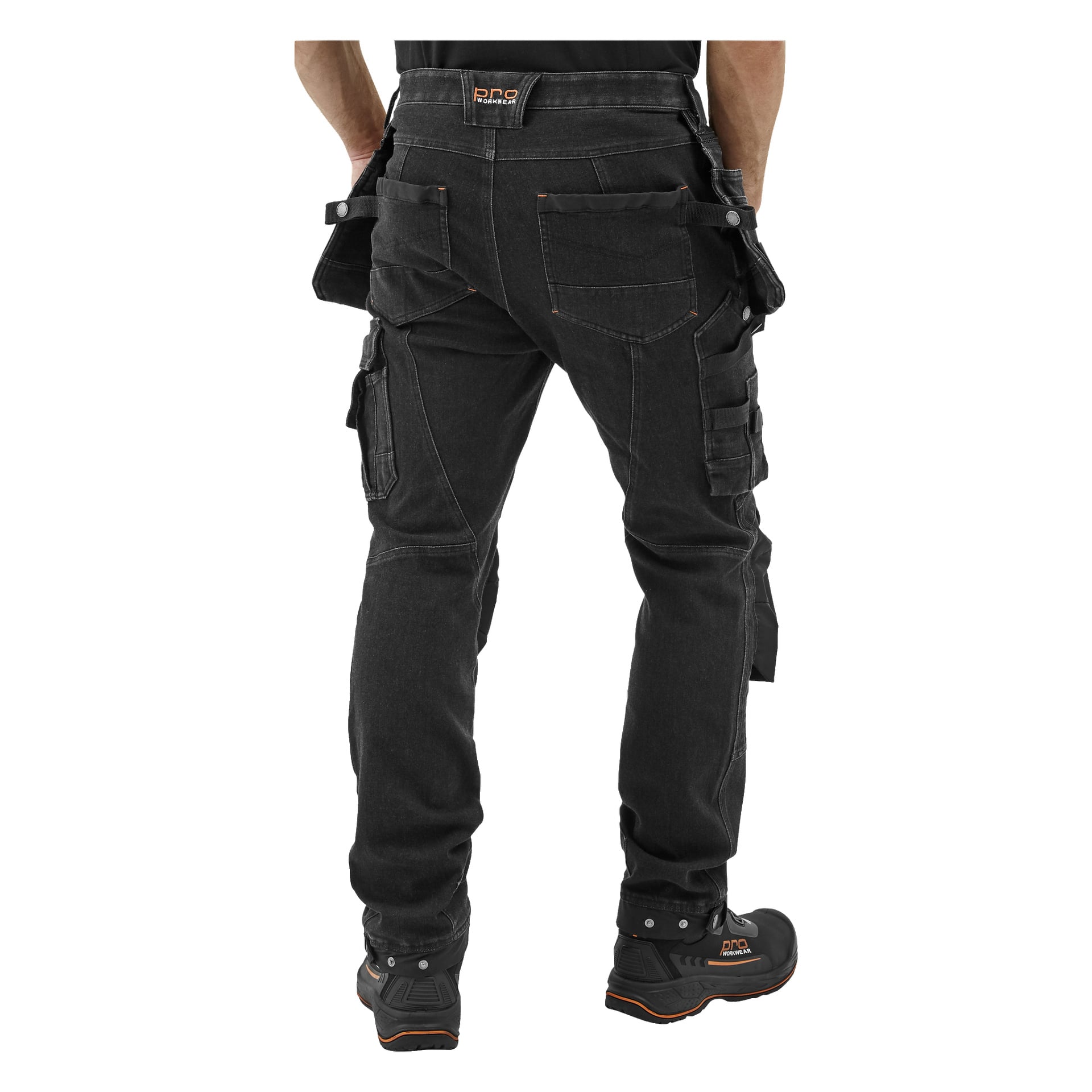En person ses bakifrån iförd Bluewear Pro Workwear Steve Denim herrbyxor med flera fickor, tillsammans med svarta arbetsstövlar.