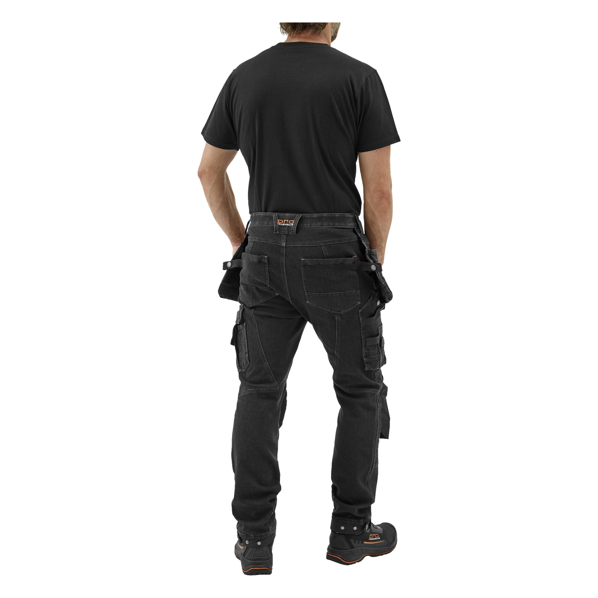 En person syns bakifrån, klädd i svart T-shirt, svarta Bluewear Pro Workwear Steve Denim herrbyxor med flera fickor och öglor, samt svarta arbetsskor med orange detaljer. En logotyp syns på byxlinningen.