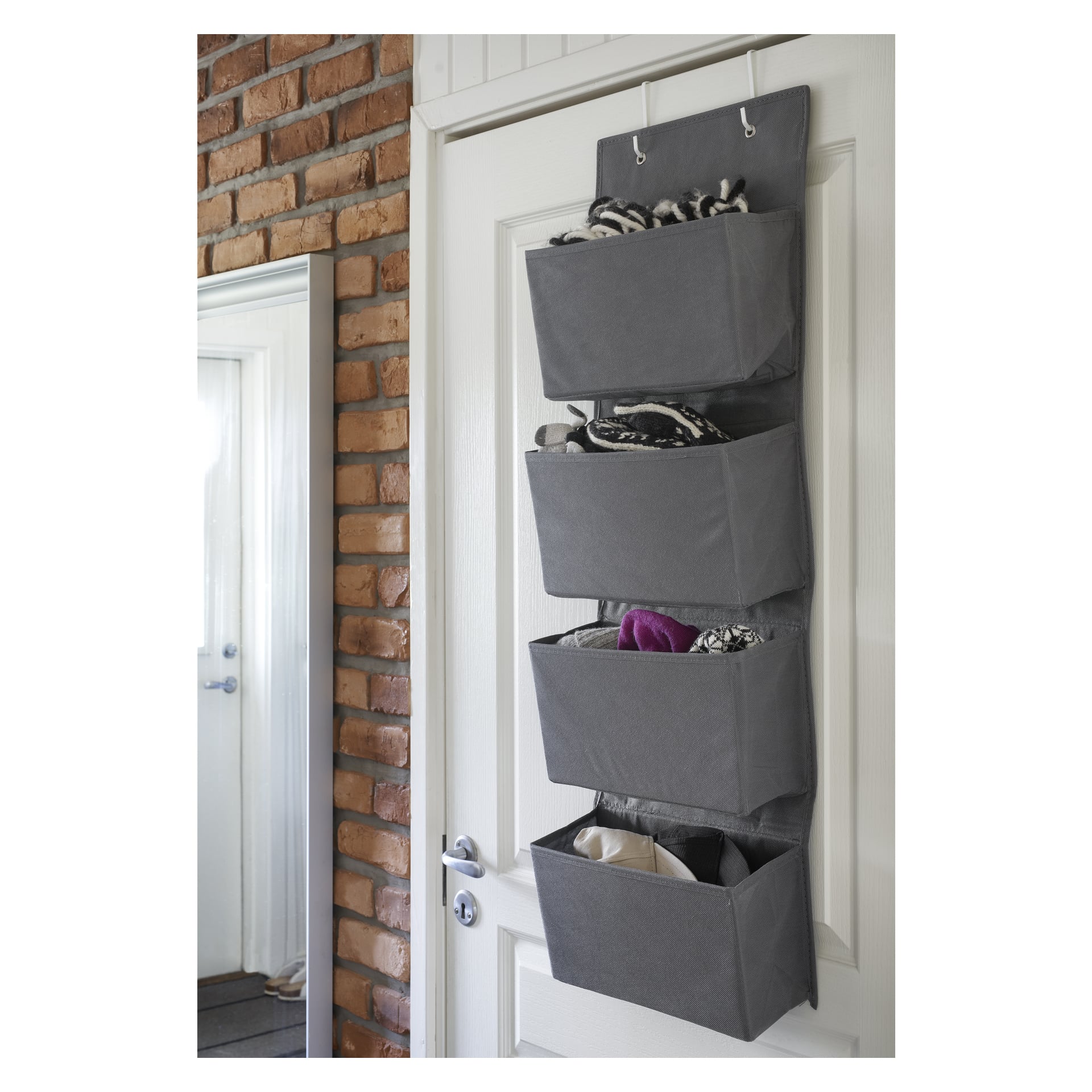 Et grått stoff Hanging Storage fra Hard Head med fire lommer er festet til en dør og oppbevarer ting som stoff, klær og tilbehør. I bakgrunnen er det en murvegg og et speil.