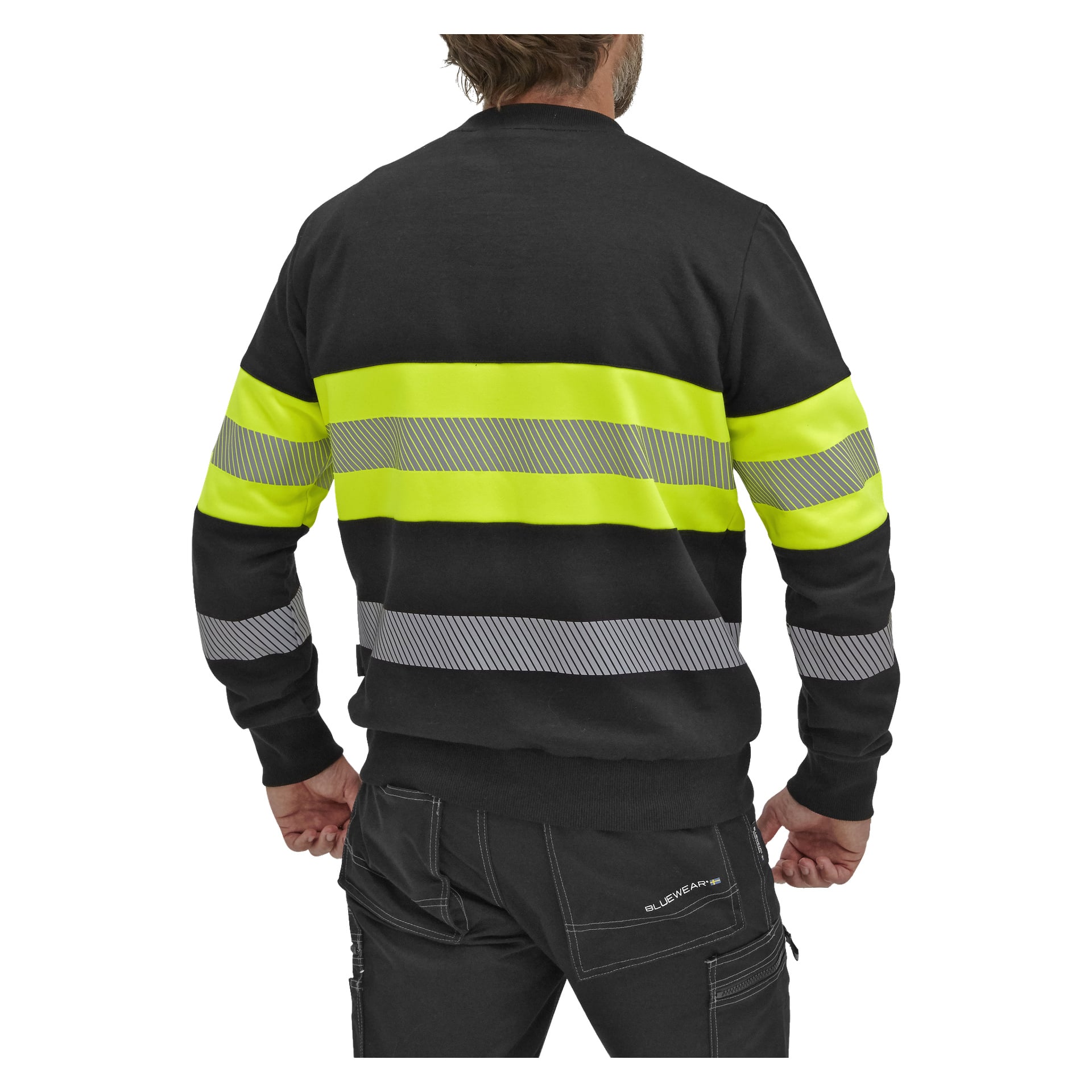 Sett bakifrån bär man Bluewear Hi-vis Vancouver-sweatshirten, som har två horisontella reflekterande gula och grå ränder över både övre och nedre ryggen, tillsammans med svarta byxor med vita sömmar.