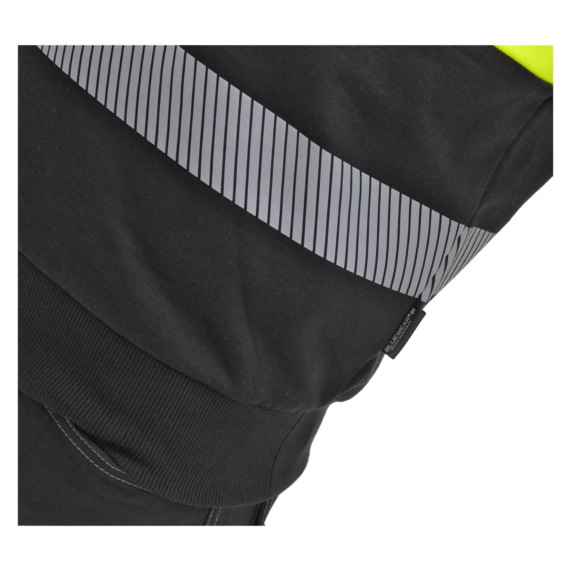 En detaljerad vy av Bluewear Hi-vis sweatshirt Vancouver framhäver dess svarta material, ett diagonalt grått randigt reflekterande band och en klar neongul sektion. Det finns också en liten svart lapp med vit text sydd i sömmen.