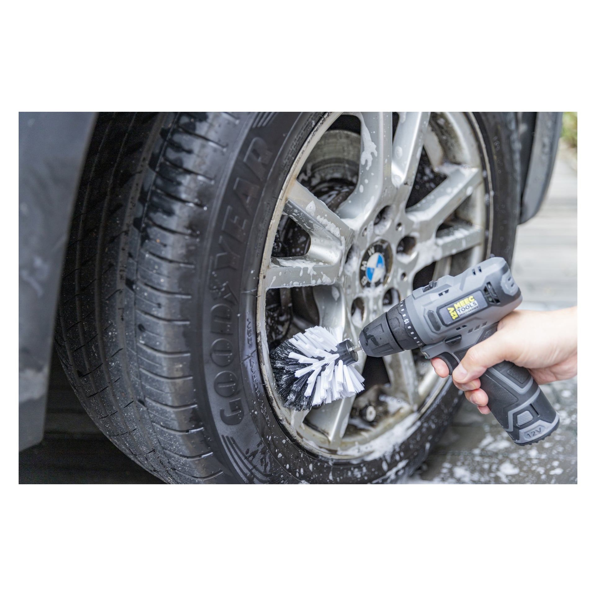 Man använder ett Meec Tools tredelat borstset kopplat till en borr för att skrubba det våta, tvåliga däcket på en Goodyear och ratten på en BMW.