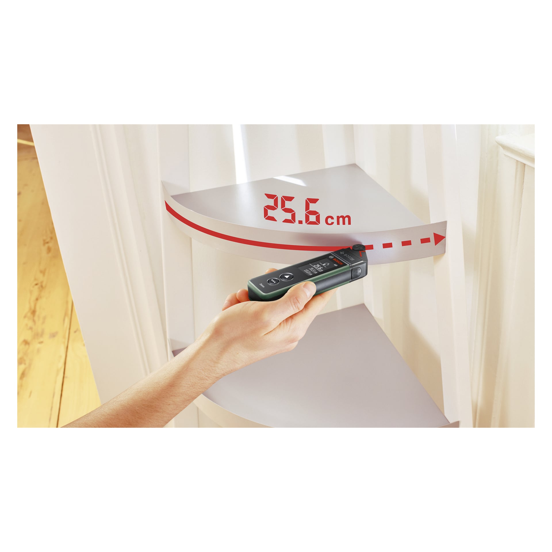 En hand håller Bosch Wheel-adaptern för Zamo IV, som visar en röd streckad linje projicerad på en böjd hylla och visar ett uppmätt avstånd på 25,6 cm.