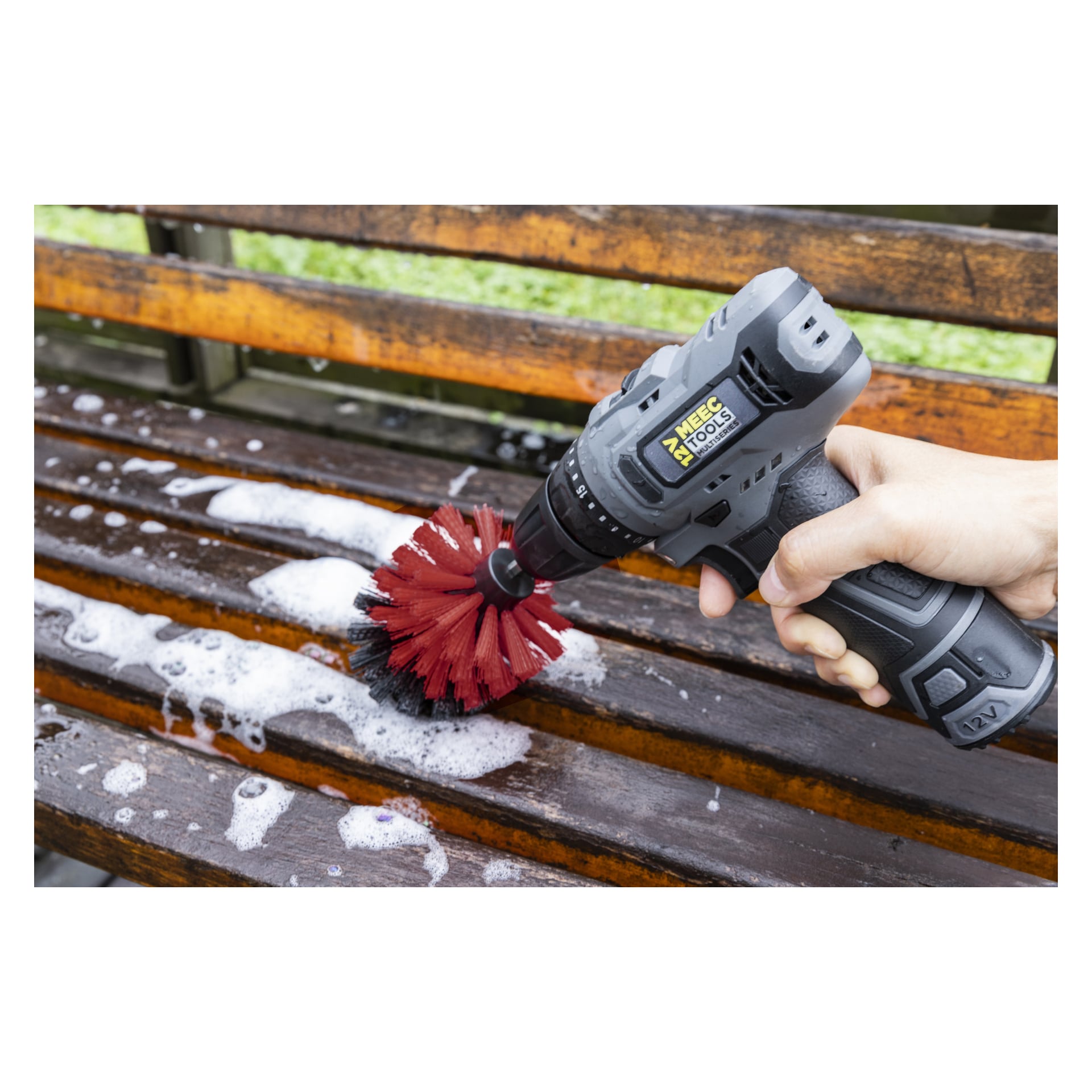 En hand använder ett Meec Tools Brushset (3-delat) fäst vid en borrmaskin för att skrubba en träbänk utomhus. Bänken täcks med tvålskum och vatten under rengöringen.