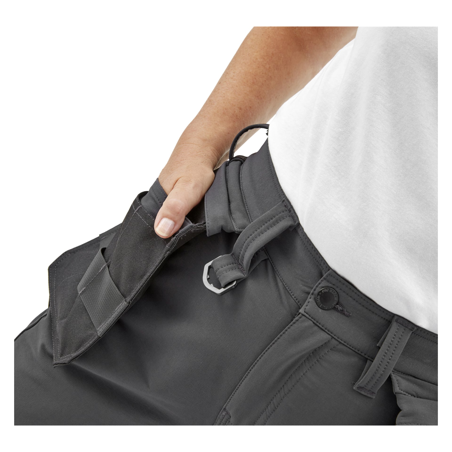 Henkilö, joka pukeutuu Bluewear Pro Workwear Women's Stella -työhousuihin ja valkoiseen paitaan, vetää irrotettavan taskun, paljastaen piilotetun vetoketjun ja harmaan soljen vyötärönauhassa.