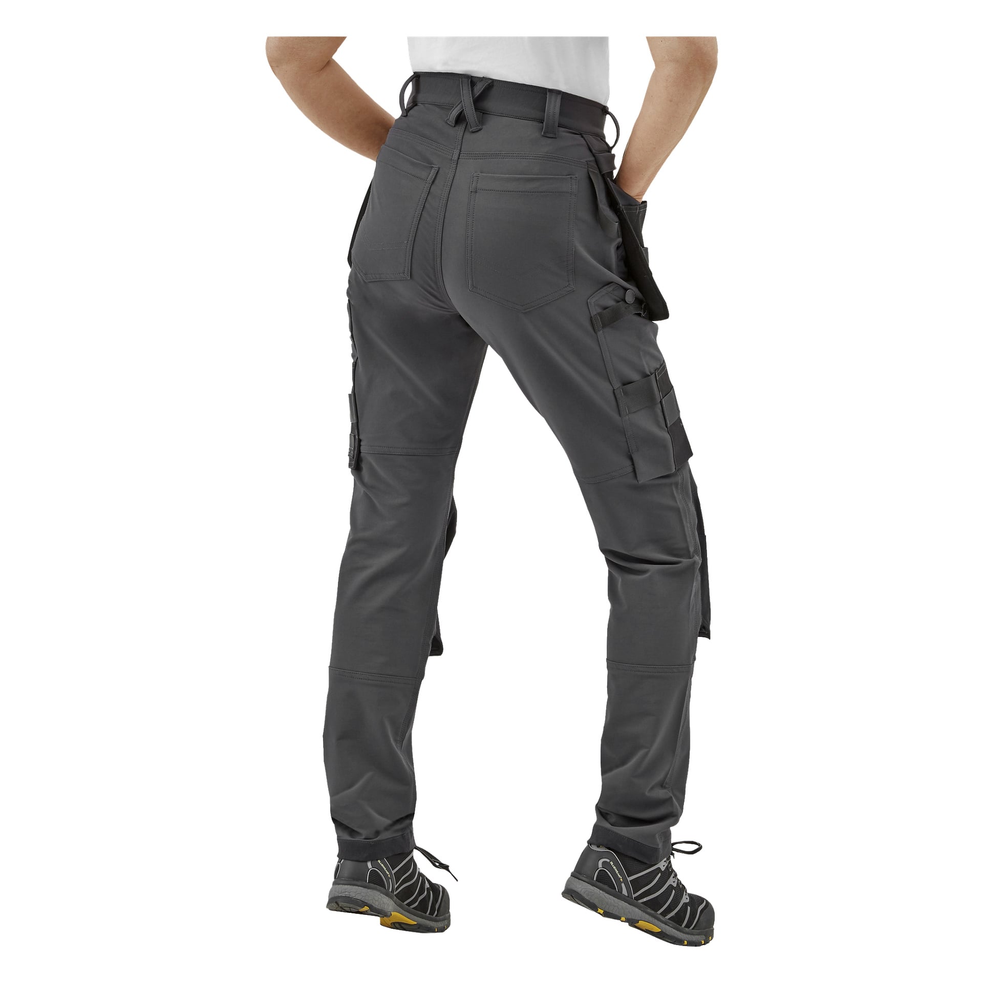 Henkilö näkyy takaa Bluewear Pro Workwear Women's Work -housuissa, Stella harmaissa, joissa on käyttölenkit ja useita taskuja, mustat ja keltaiset kengät sekä valkoinen paita.
