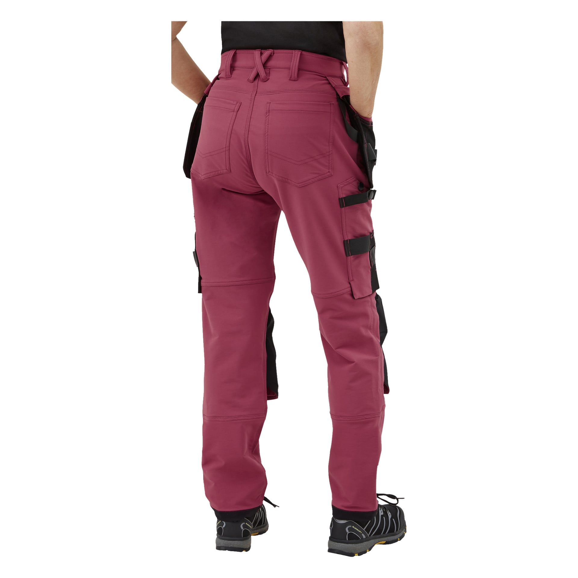 Personen med ryggen bort, klädd i röda Bluewear Pro Workwear Dambyxor Stella med svarta fickor och sidoremmar. Fokus ligger på byxans baksida och ben.