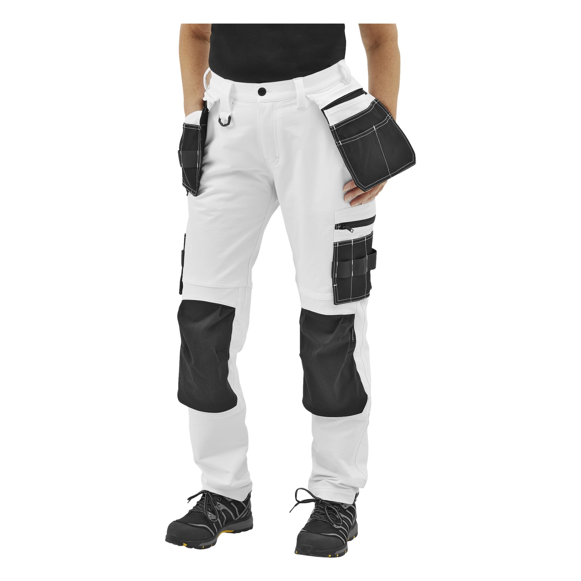 En person visas från midjan och ner bär Bluewear Pro Workwear Women's work pants Stella, med svarta förstärkta knäskydd, svarta fickor och svarta arbetsskor.
