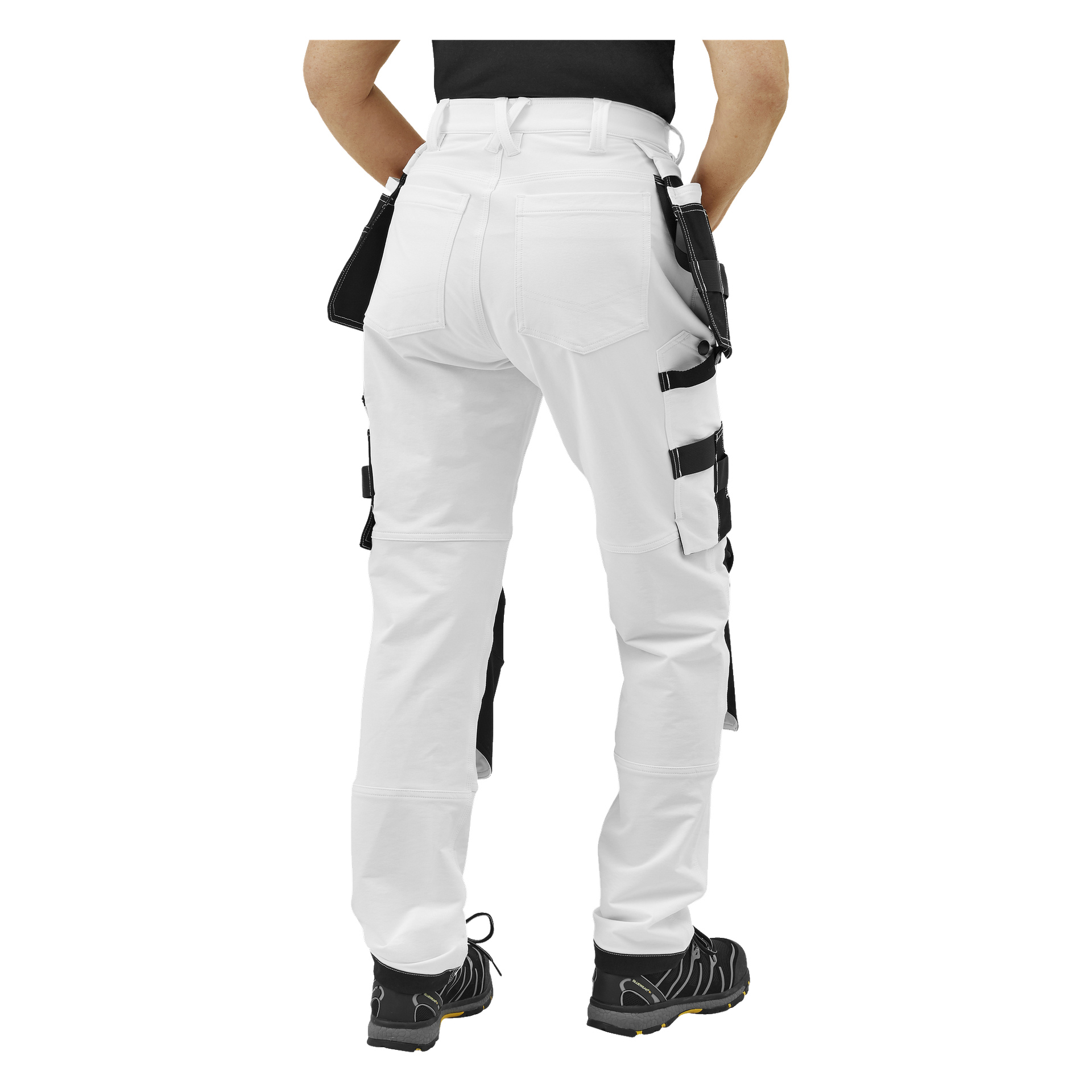Person vänd bort från kameran, klädd i damarbetsbyxor Stella från Bluewear Pro Workwear—vita byxor med svarta fickor och verktygsöglar, en svart skjorta och svarta arbetsskor med gula detaljer.