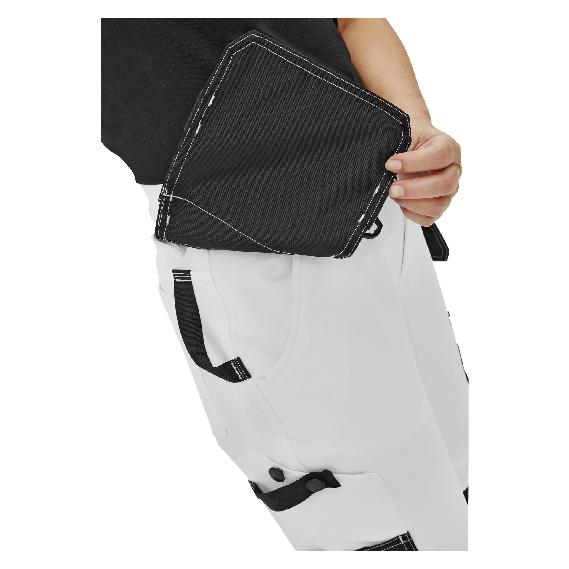 En person, synlig från bålen och neråt, placerar eller tar ut en svart knäskydd ur framfickan på sina Bluewear Pro Workwear Women's work pants Stella. Personens hand och en del av överkroppen syns.
