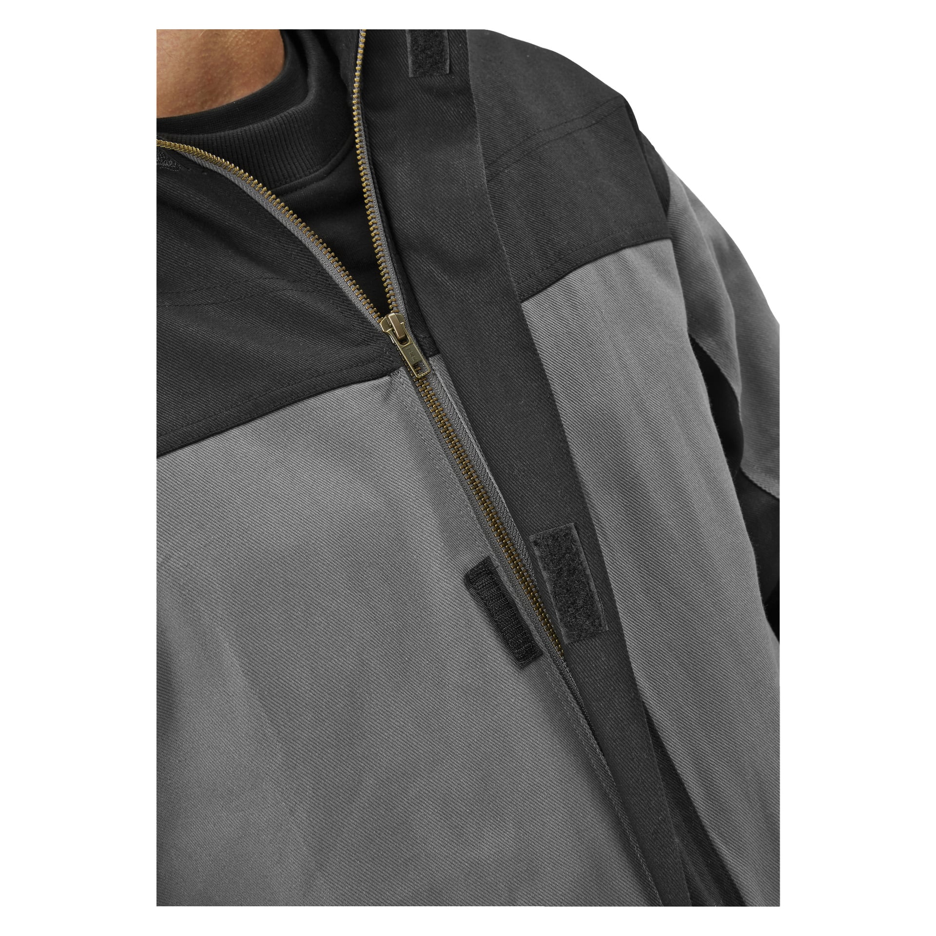 Nærbilde av Bluewear Mens arbeidsoveraller Owe i grått og svart, med messingglidelås og svarte krokelåser, laget av solid materiale. Overallen bæres over en svart skjorte, med kun overkroppen synlig.