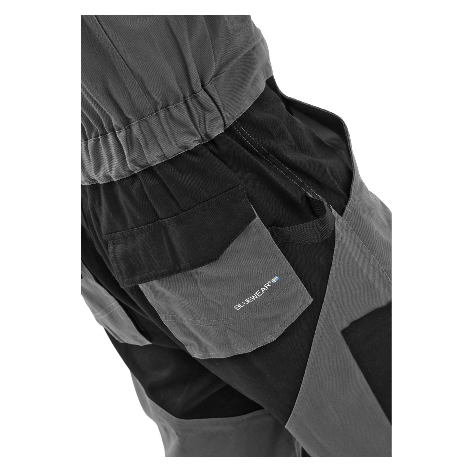 Närbild på en person i herrarbetsoveraller Owe by Bluewear, med svart och grått tyg med flera fickor och en etikett där det står Bluewear tillsammans med en blå-gul flagga.