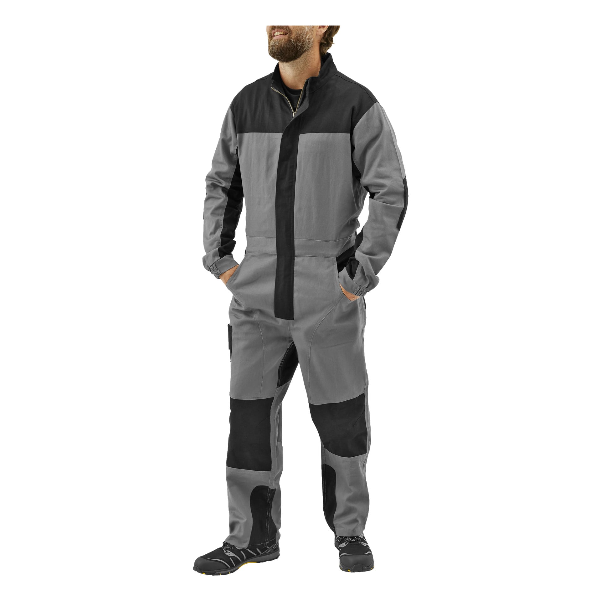 En man bär herrarbetsoveraller Owe by Bluewear med händerna i fickorna, lite åt vänster. Den grå kostymen har svarta märken på axlar, armar, knän och underben. Han har svarta skor.