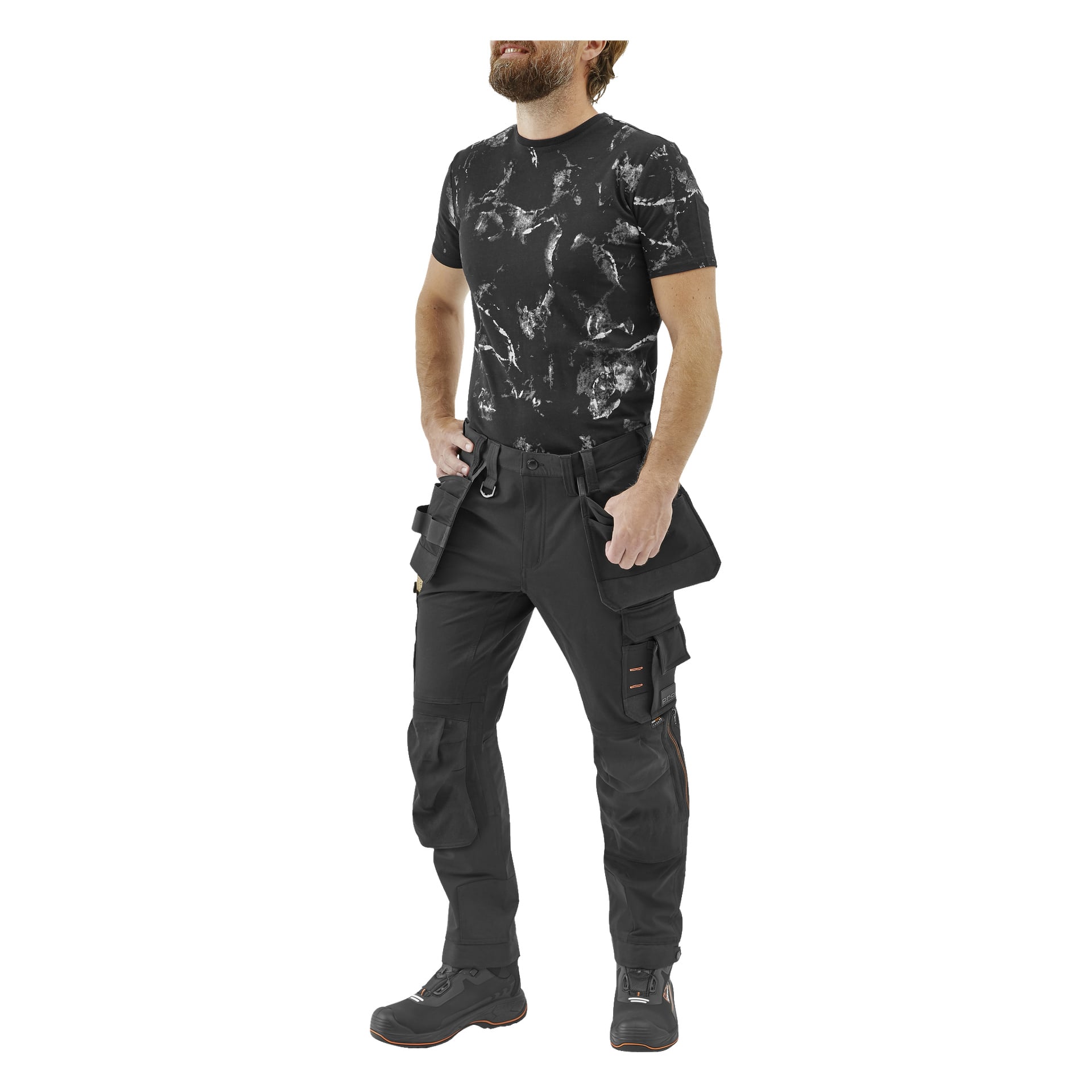 En skäggig man står vänd åt vänster, händerna i sidorna och ler. Han har på sig en svart marmorerad t-shirt, Bluewear Pro Workwear arbetsbyxor för herrar, Steve och svarta arbetsstövlar.