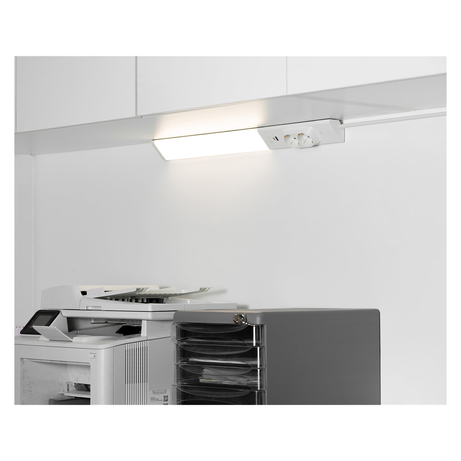 En Anslut Worktop LED-lampa är tänd ovanför en vit kontorskopiator och en svart papperssorterare med flera fack, båda placerade nära skåpen i ett starkt upplyst kontor.