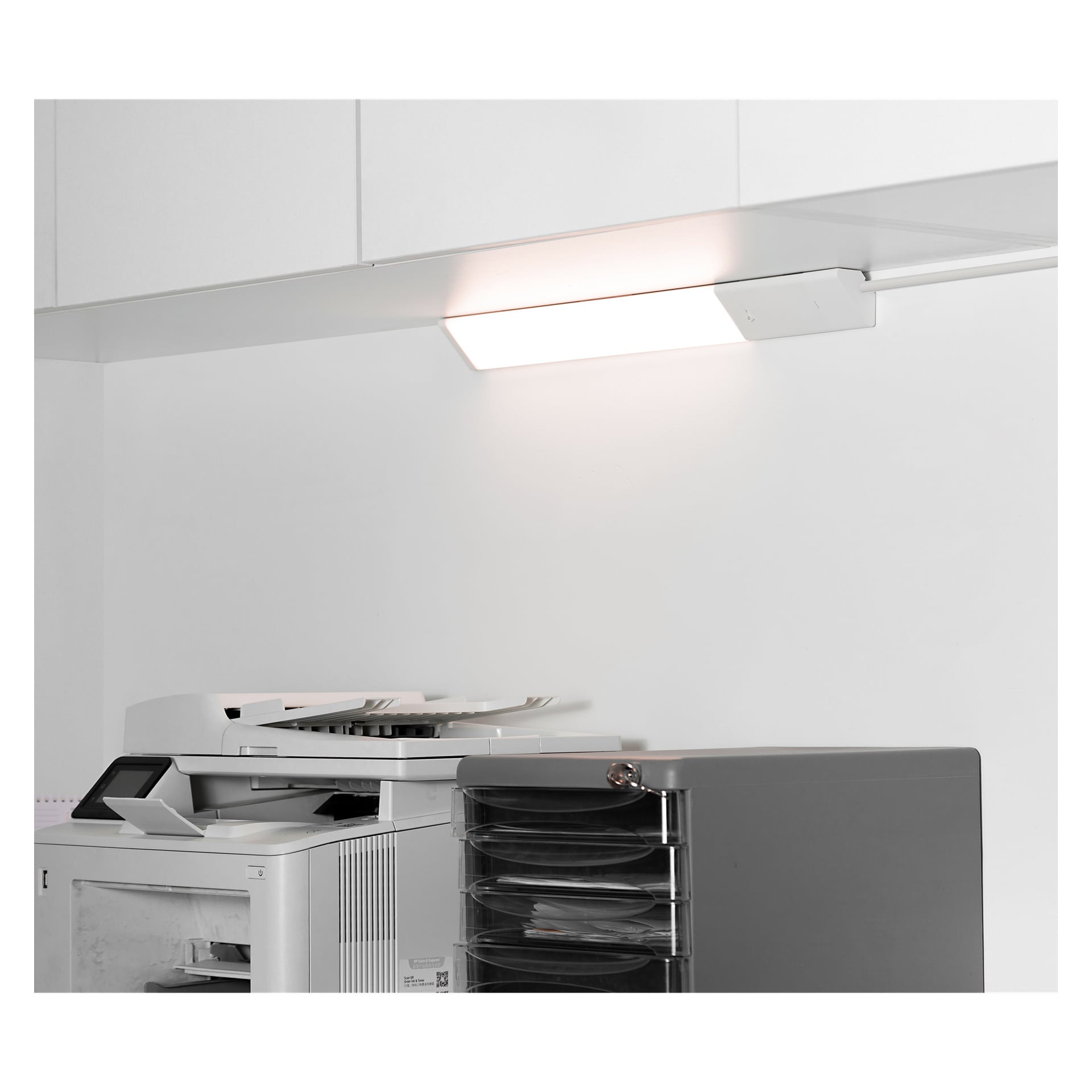 En kopiator och en svart papperssorterare står under en Anslut Worktop, LED-lampa och vita skåp.