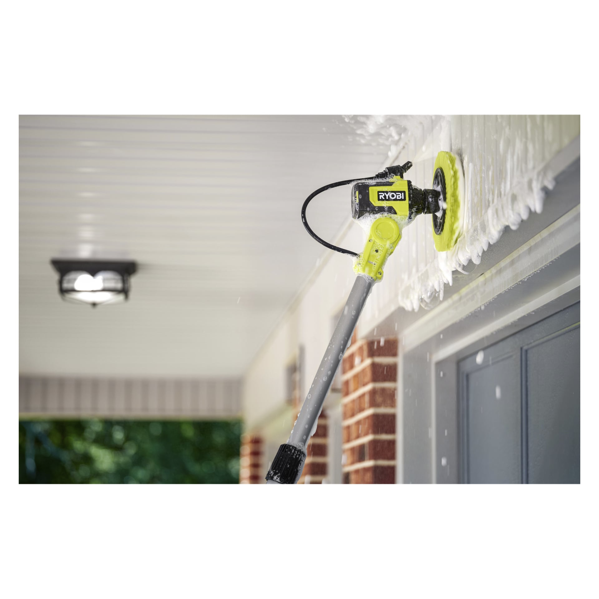 En Ryobi One+ Ring-borste med långt handtag skrubbar den vita taklisten ovanför en verandadörr, med tvålskum synligt runt det snurrande borsthuvudet.