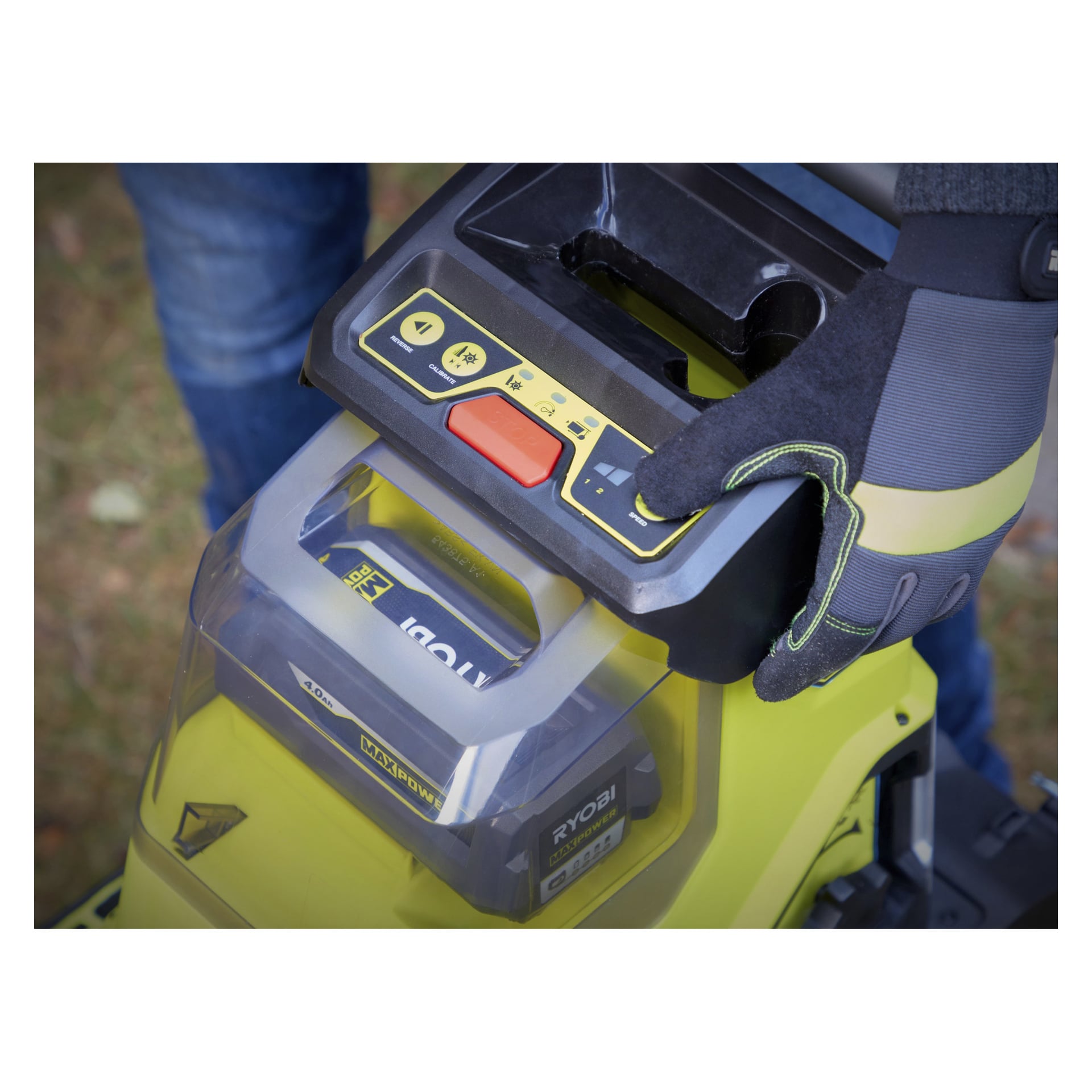 En handskbeklädd hand trycker på en knapp på kontrollpanelen på en Ryobi Max Power RY36SHX40-0 batteridriven kompostförstörare med batteripaketet tydligt synligt.
