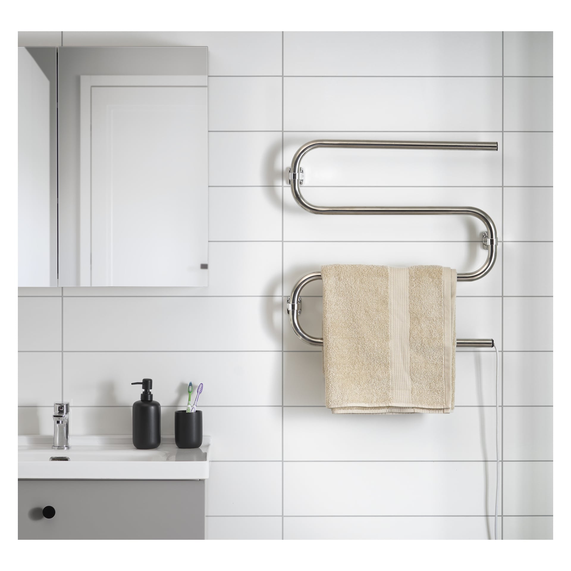 Ett badrum med vita kakelväggar, ett spegelskåp ovanför en elegant handfat, svarta tvåldispensrar, två tandborstar och en EKVIP uppvärmd handduksräck med en beige handduk.