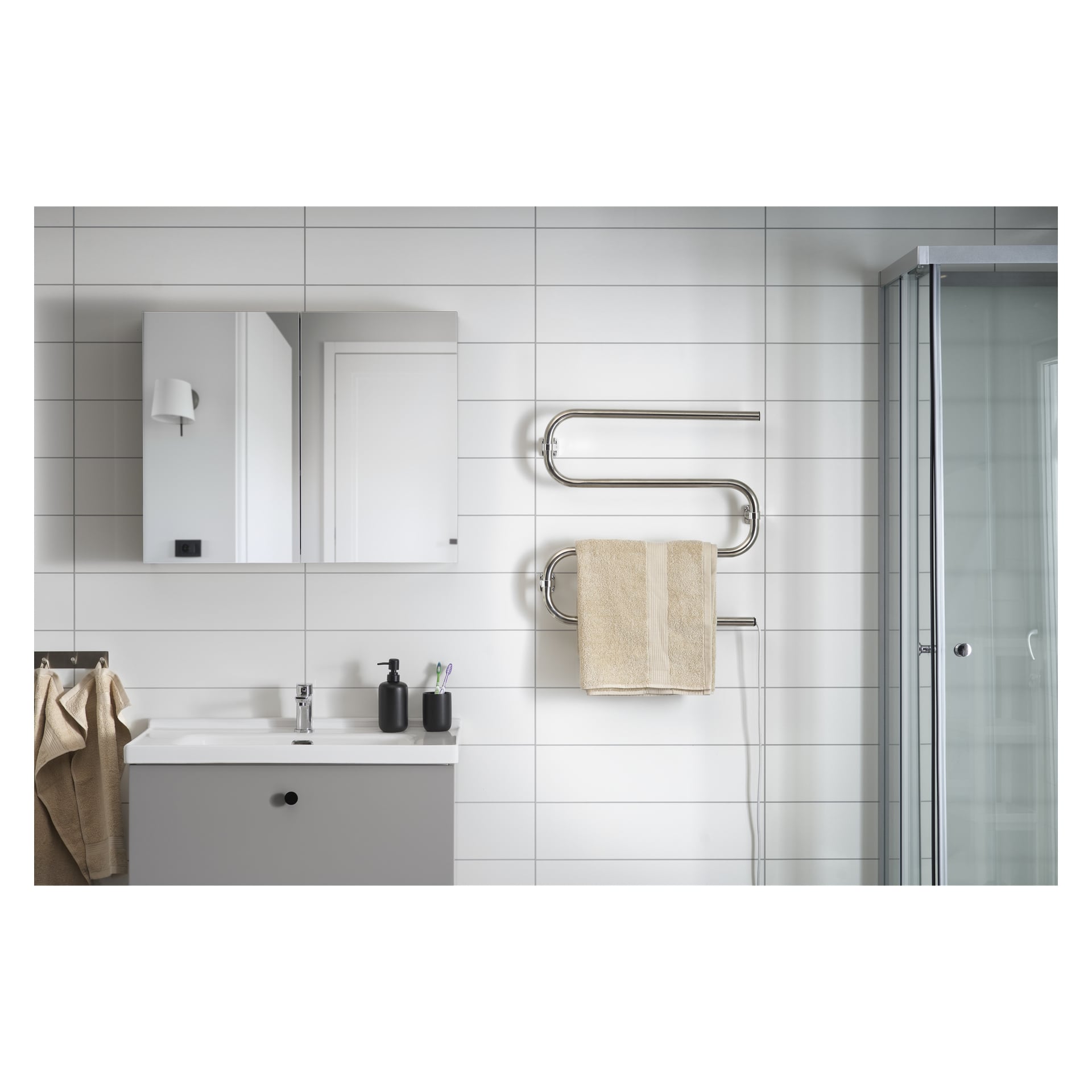 Modern badrum med vit kaklad vägg, grå sminkbord, spegelskåp, EKVIP uppvärmd handduksräck med beige handduk, tvåldispenser och glasdusch till höger. Neutrala färger och minimalistisk inredning.