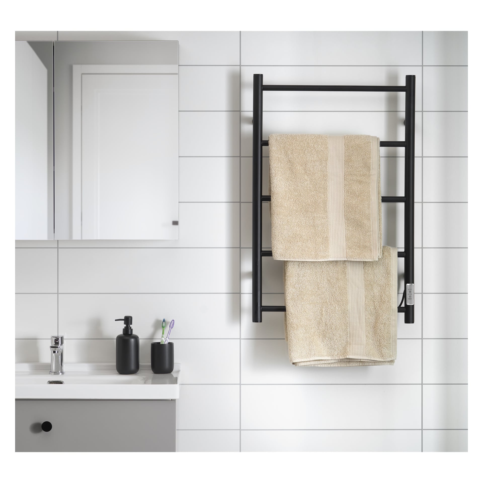 Badrummet har vitt kakel, svart handdukshängare med två beige handdukar, väggspegel, vitt handfat med svart tvålpump och en kopp tandborstar.