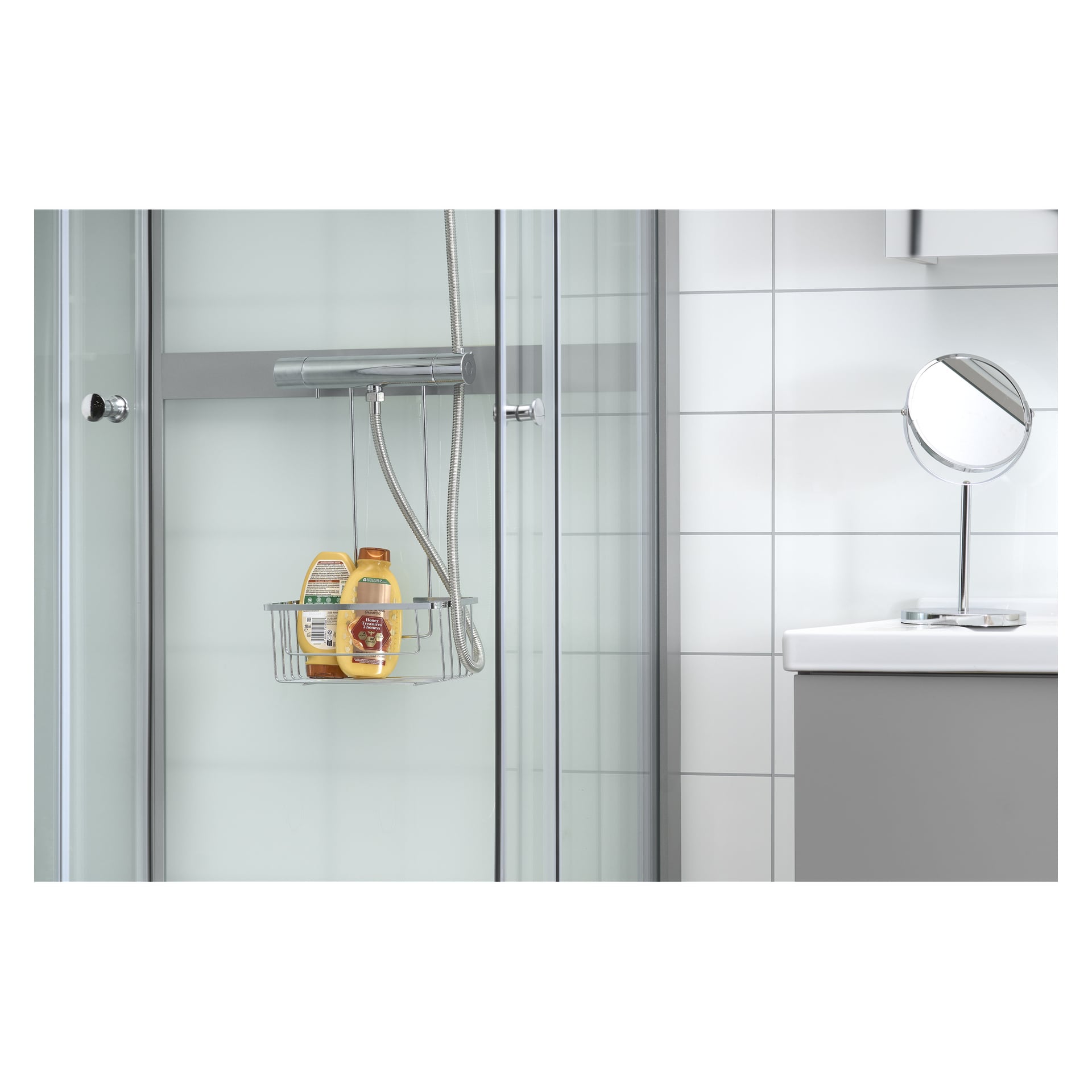 En elegant duschuppsättning visar upp EKVIP Shower-hyllan med tre flaskor instoppade bakom en glasdörr och en silverfärgad handdusch. Till höger finns en vit kaklad vägg, en diskbänk och en rund spegel.