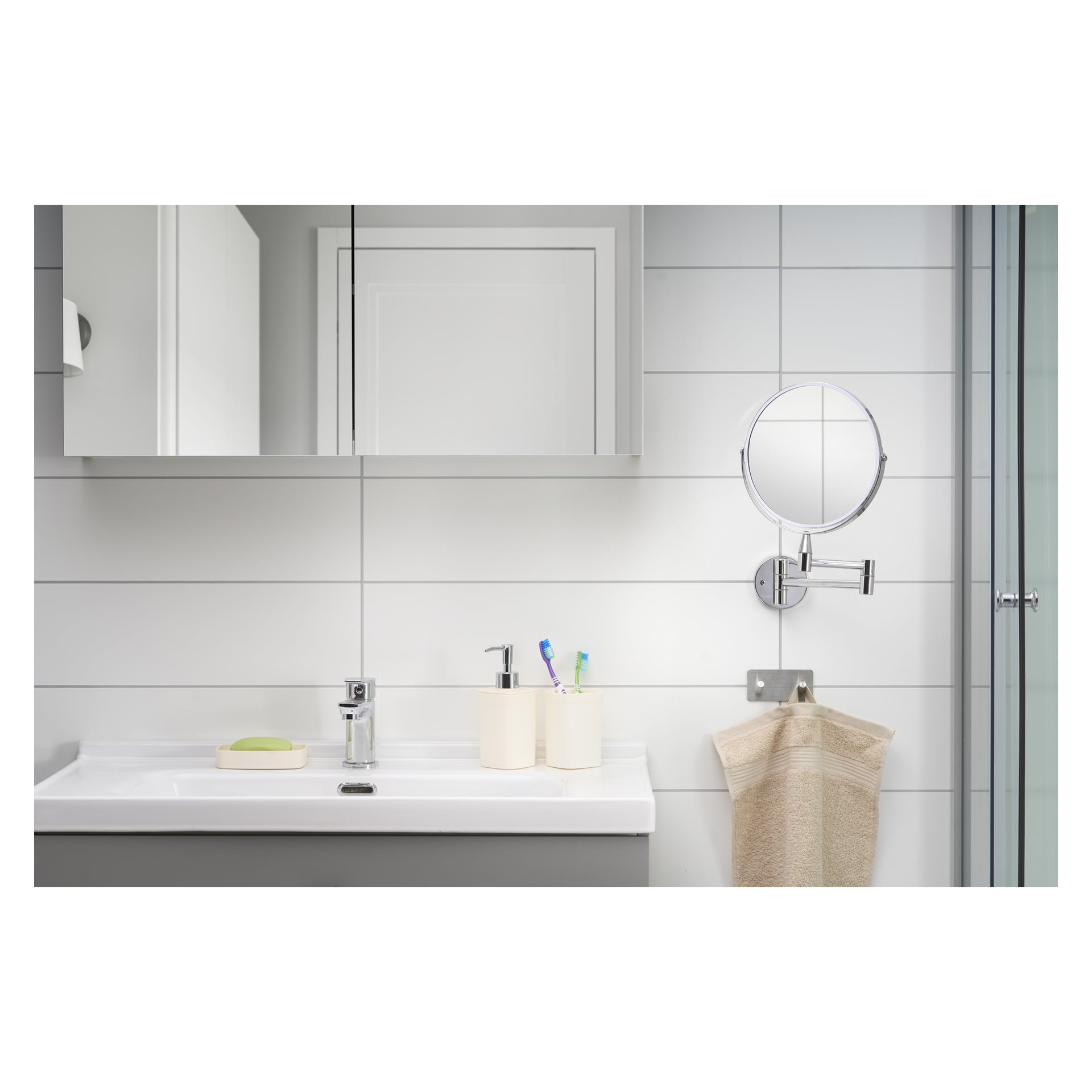 En EKVAP-spegel hänger över ett modernt badrumshandfat, tillsammans med en tvålskål, en hållare med tandborstar, en pumptvålautomat och en beige handduk draperad vid sidan. Väggen bakom diskhon har vit kakel.