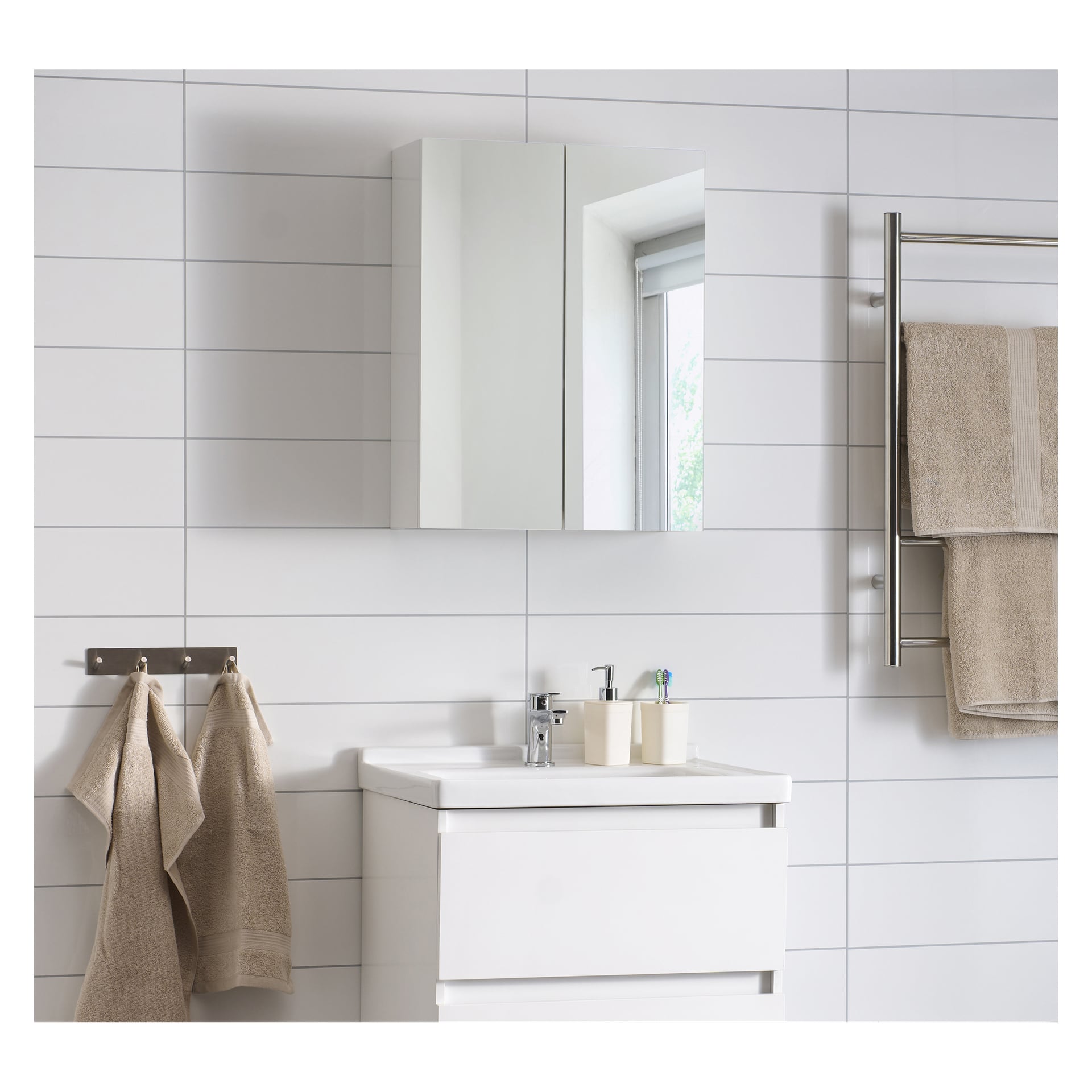Ett badrum med ett EKVIP-spegelskåp på väggen ovanför ett vitt diskbänkskåp, beige handdukar prydligt arrangerade på ställningar och ett fönster synligt i spegelns reflektion. Väggarna är klädda med horisontella vita plattor och tunna grå detaljer.