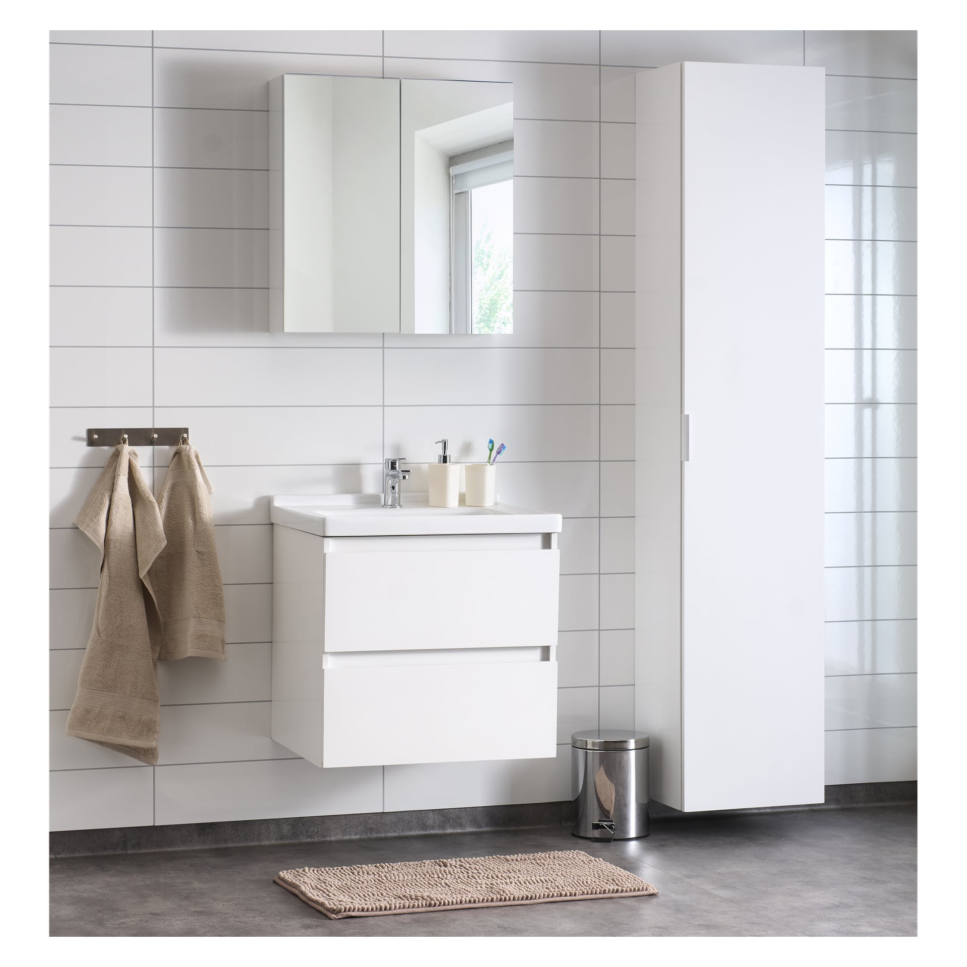Ett modernt badrum visar upp EKVIP Badrumsset Girona, inklusive strömlinjeformade vita skåp, en flytande handfat och ett spegelriktat medicinskåp. Beige handdukar placeras prydligt på ett väggställ ovanför en metallavfallsbehållare, medan en vävd matta ligger ovanpå det grå kakelgolvet. Rummet lyser upp av vita kaklade väggar och naturligt ljus som strömmar in genom ett fönster.