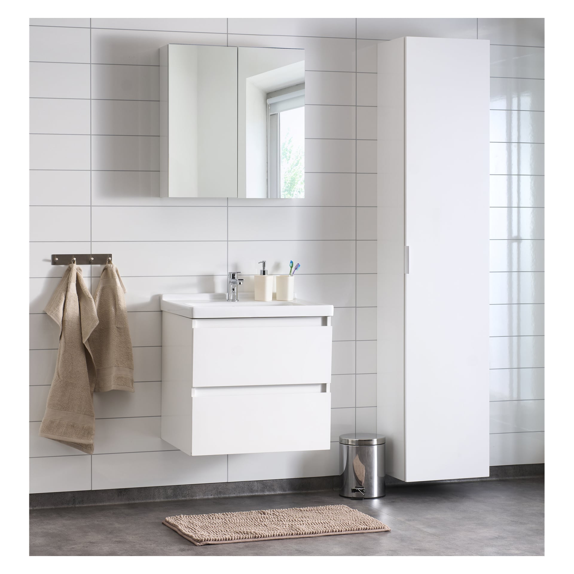 Ett modernt badrum med vita skåp, en väggmonterad handfat med två lådor, ett spegelskåp, EKVIP Tall Girona, beige handdukar prydligt upphängda på en ställning, en metallisk soptunna och en beige matta som täcker delar av det grå golvet.