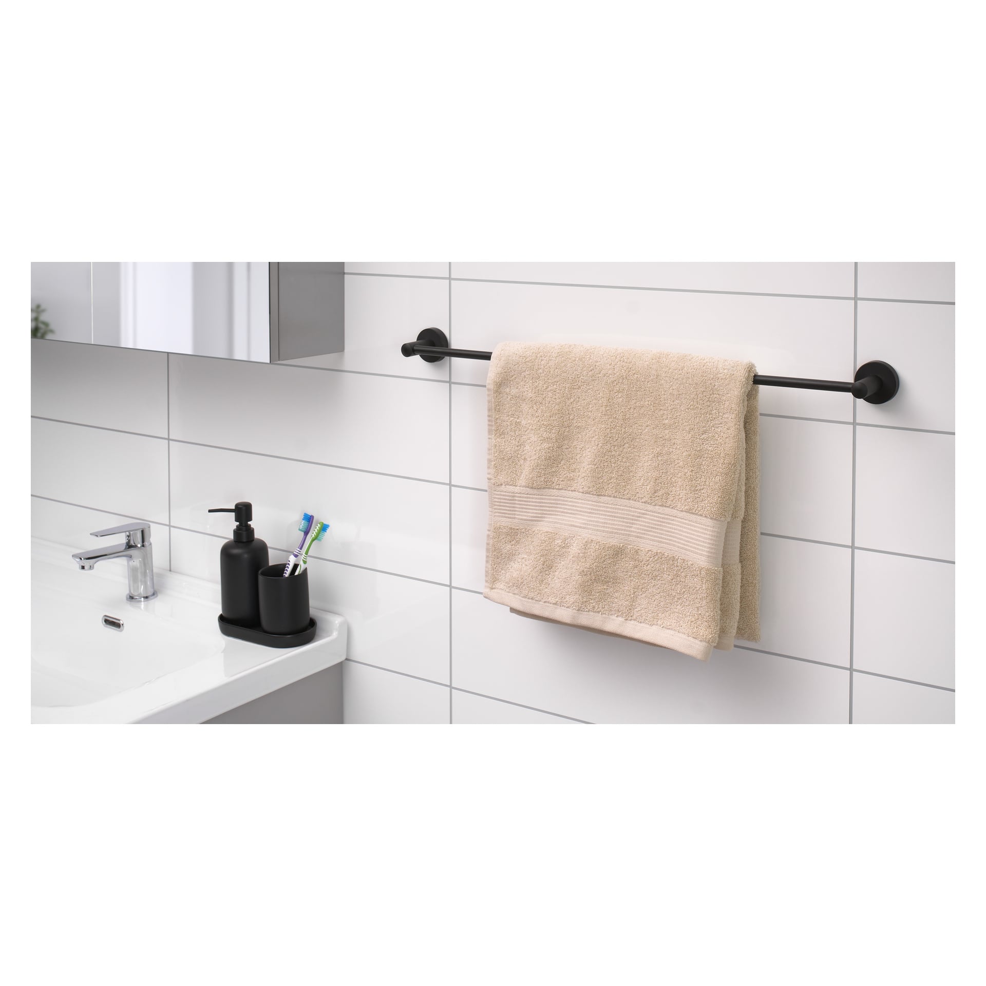 Ett svart EKVAP-handdukshänge är fäst vid en kaklad badrumsvägg och visar en beige handduk. Nedanför finns en vit handfat med en svart tvålautomat och en bricka med gröna och blå tandborstar.
