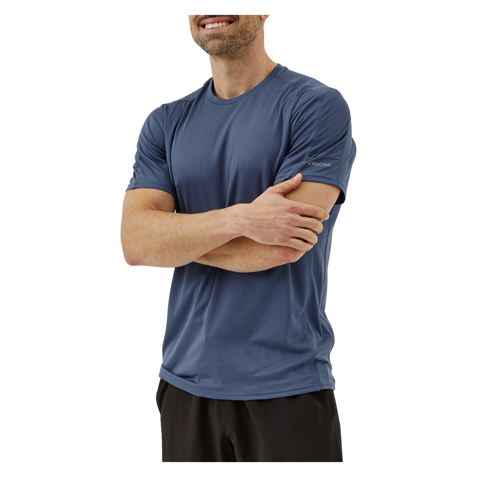En kvinna står med armarna i kors, klädd i Kayoba-kvinnornas funktionella topp och mörka byxor. Hon har ett svagt leende, och bara en del av hennes ansikte syns.