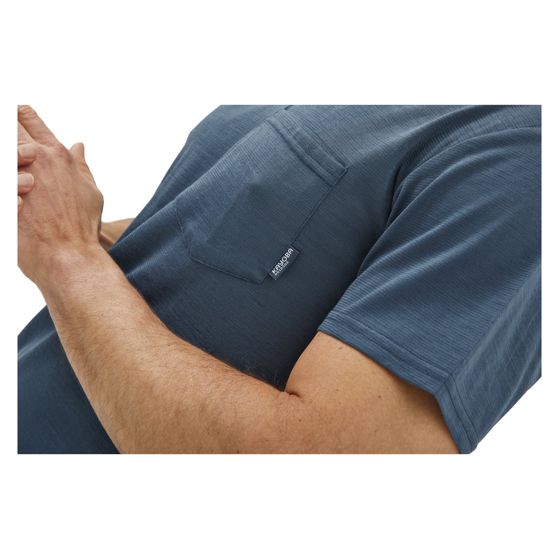 Man visar Kayoba Women's blå funktionella topp, som har kortärmat, bröstficka och en liten "Kunskap"-etikett. Bilden visar endast bålen och lätt böjda armar.