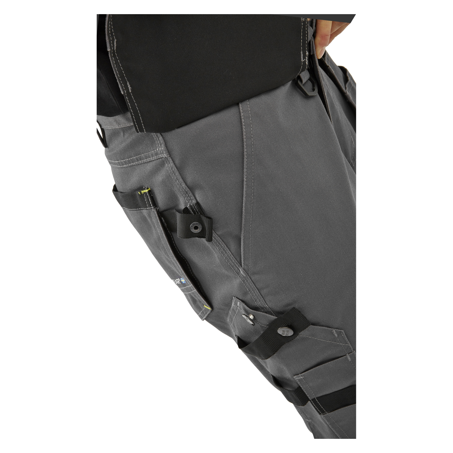 Detaljerad vy av en person klädd i Bluewear Men's Rex arbetsshorts med flera fickor, svarta remmar och verktygshållare. Personens högra hand vilar nära midjebandet, och en del av en svart skjorta är också synlig.