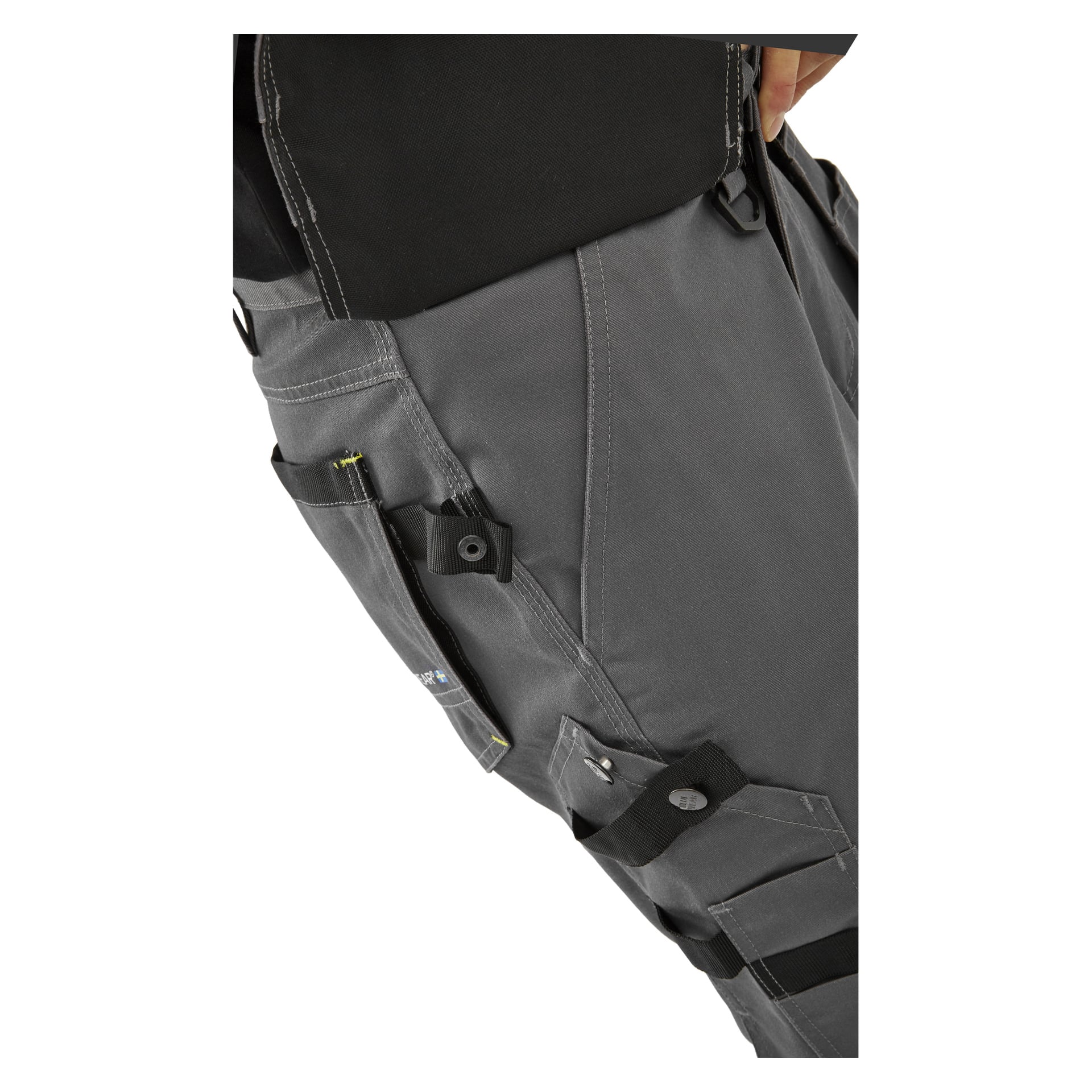 En person visas i närbild iförd Bluewear Men's Rex arbetsshorts med flera fickor och svarta remmar, där hon håller en penna eller ett verktyg i en sidoficka.