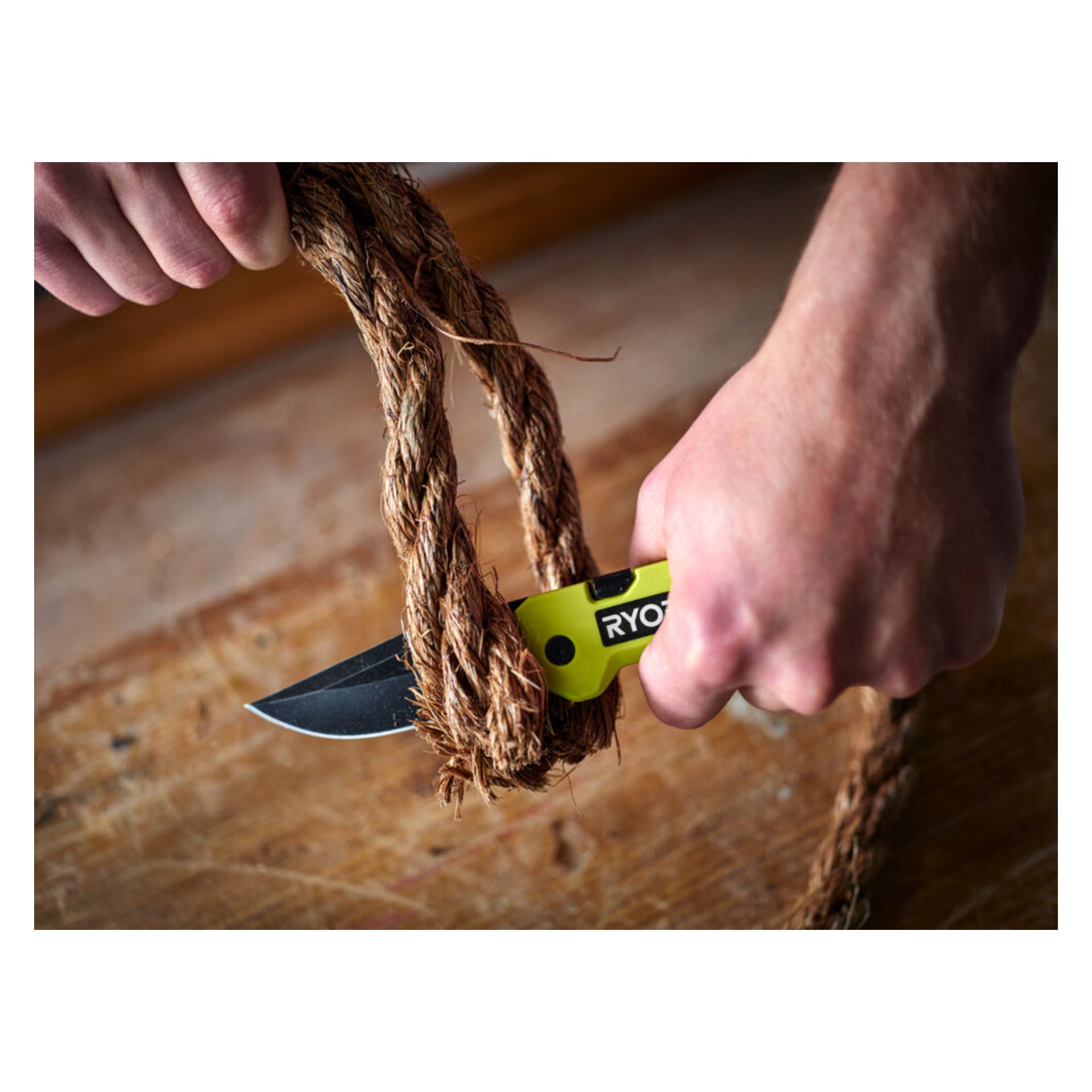 Någon skär igenom ett tjockt brunt rep med en gul och svart Ryobi Jack knife RHCKF-3 ovanpå en träyta.